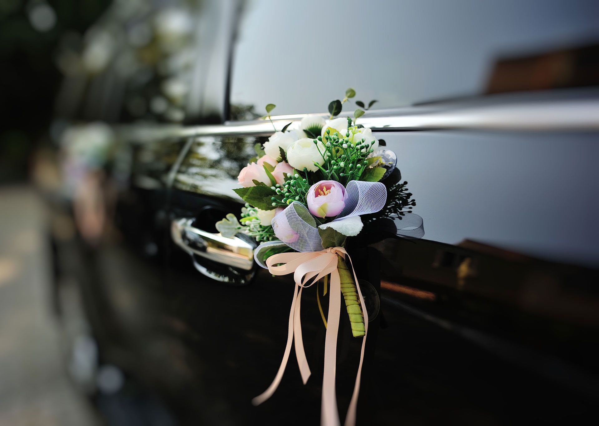 Small white and pastel flower bouquet tied to a black car door handle with pink ribbons