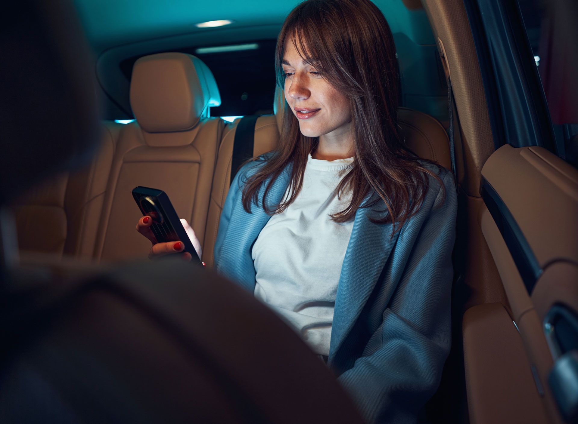 Woman seated in a car at night, looking at her phone with a faint smile