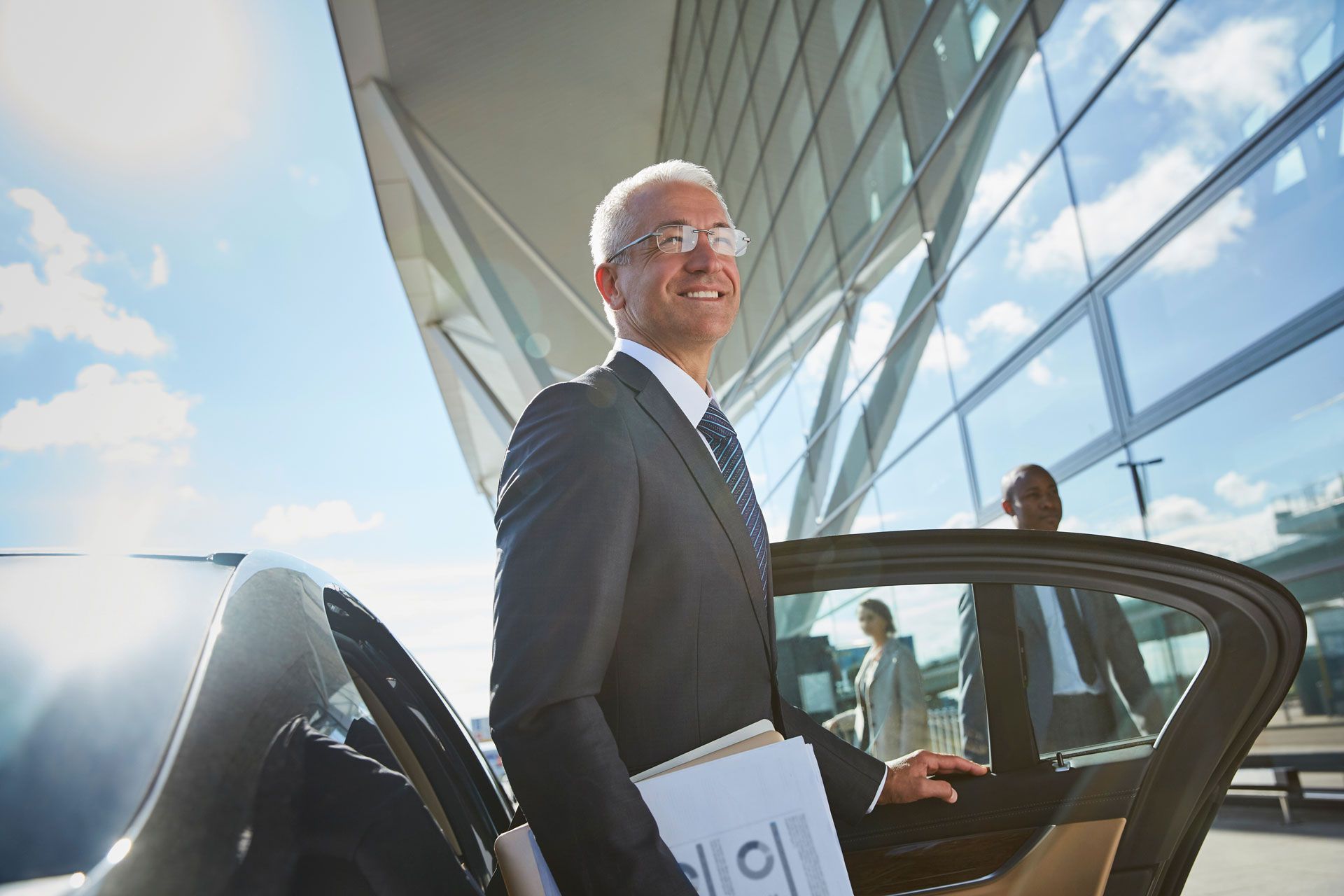 Smiling executive stepping out of a car beside a modern glass office building