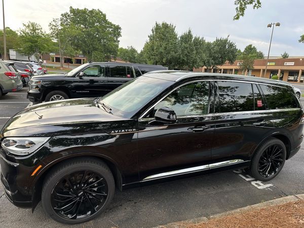 Black SUV parked in a lot beside other vehicles, with trees and buildings in the background