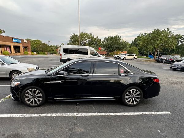 Black sedan parked in a lot with other cars and a white van under an overcast sky