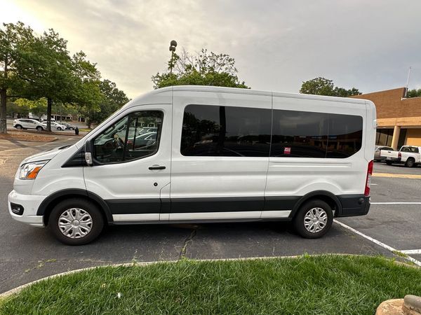 White passenger van parked in a parking lot beside a building and trees