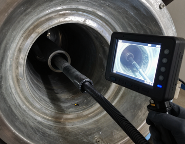 Borescope inspecting the inside of a large metal pipe, with a small screen showing the interior view.