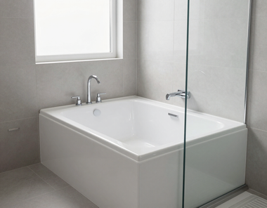 Modern white bathtub in a bright tiled bathroom with a window and glass shower panel