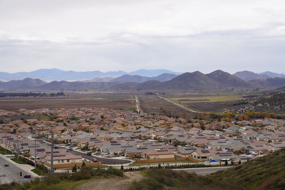 Suburban houses in a valley, with distant mountains under a cloudy sky.