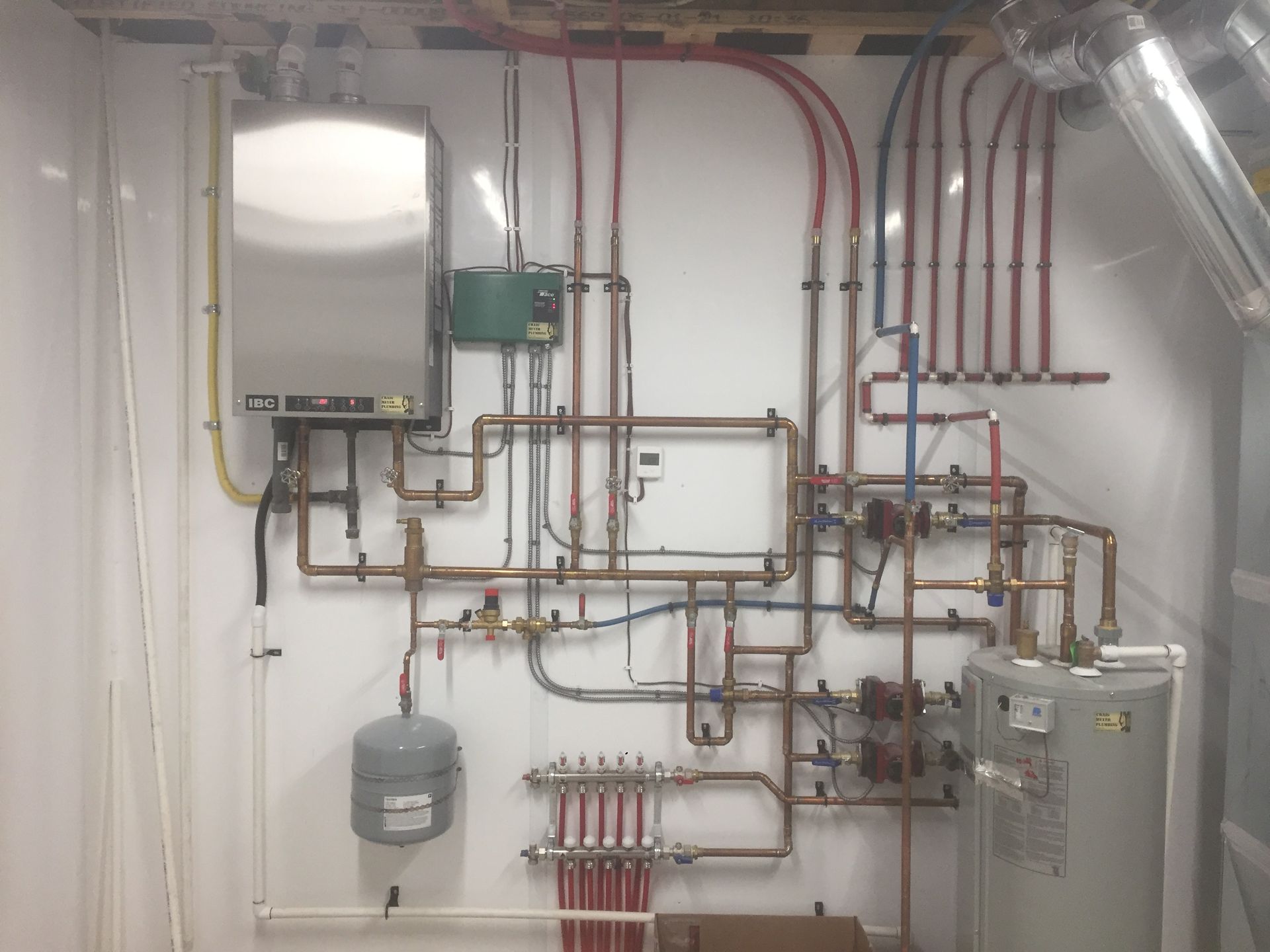 A utility room with a water heater, boiler, and complex network of copper and colored pipes.