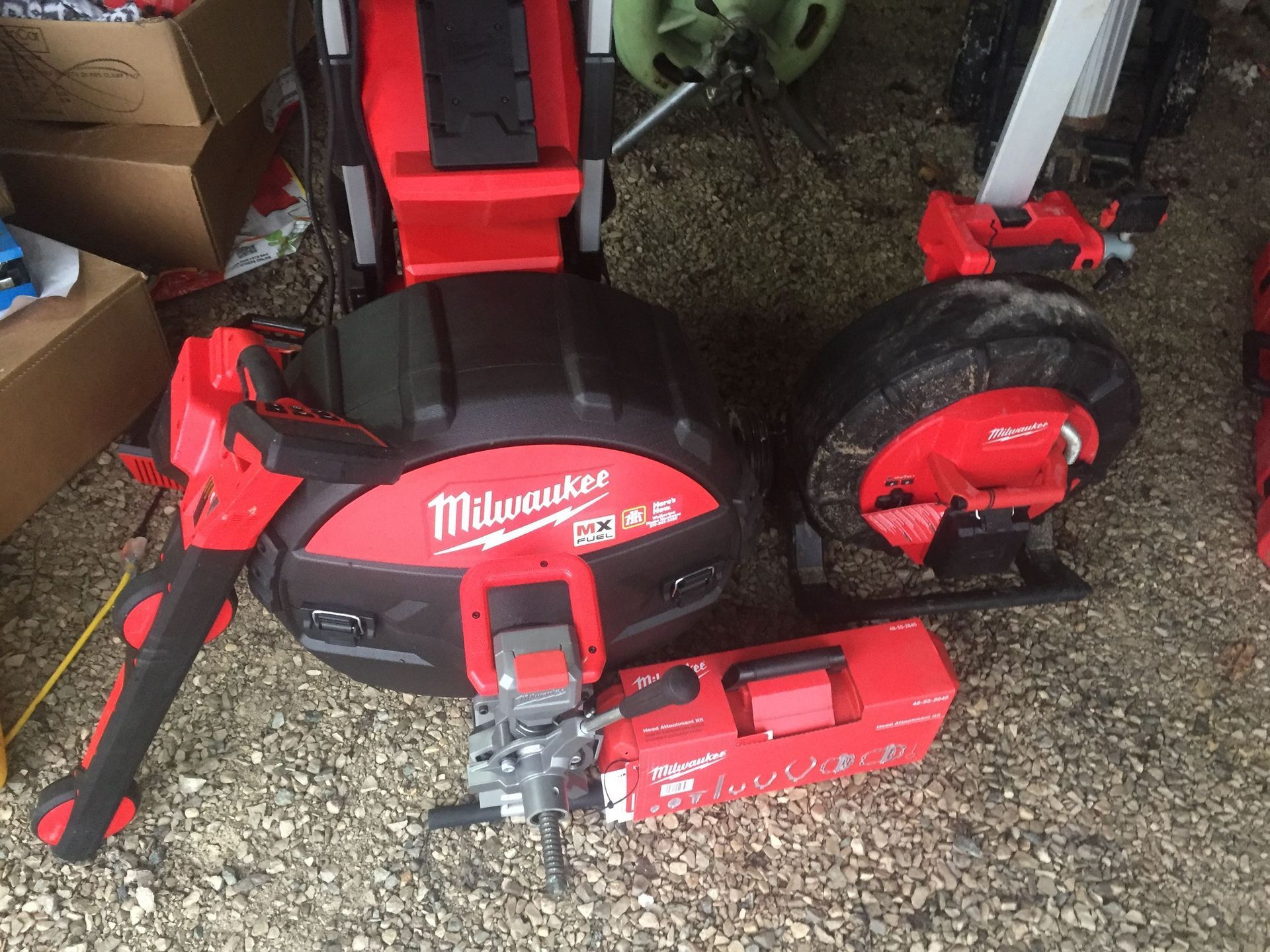 Milwaukee plumbing tools: drain cleaner, camera, and saws in red and black on a gravel surface.