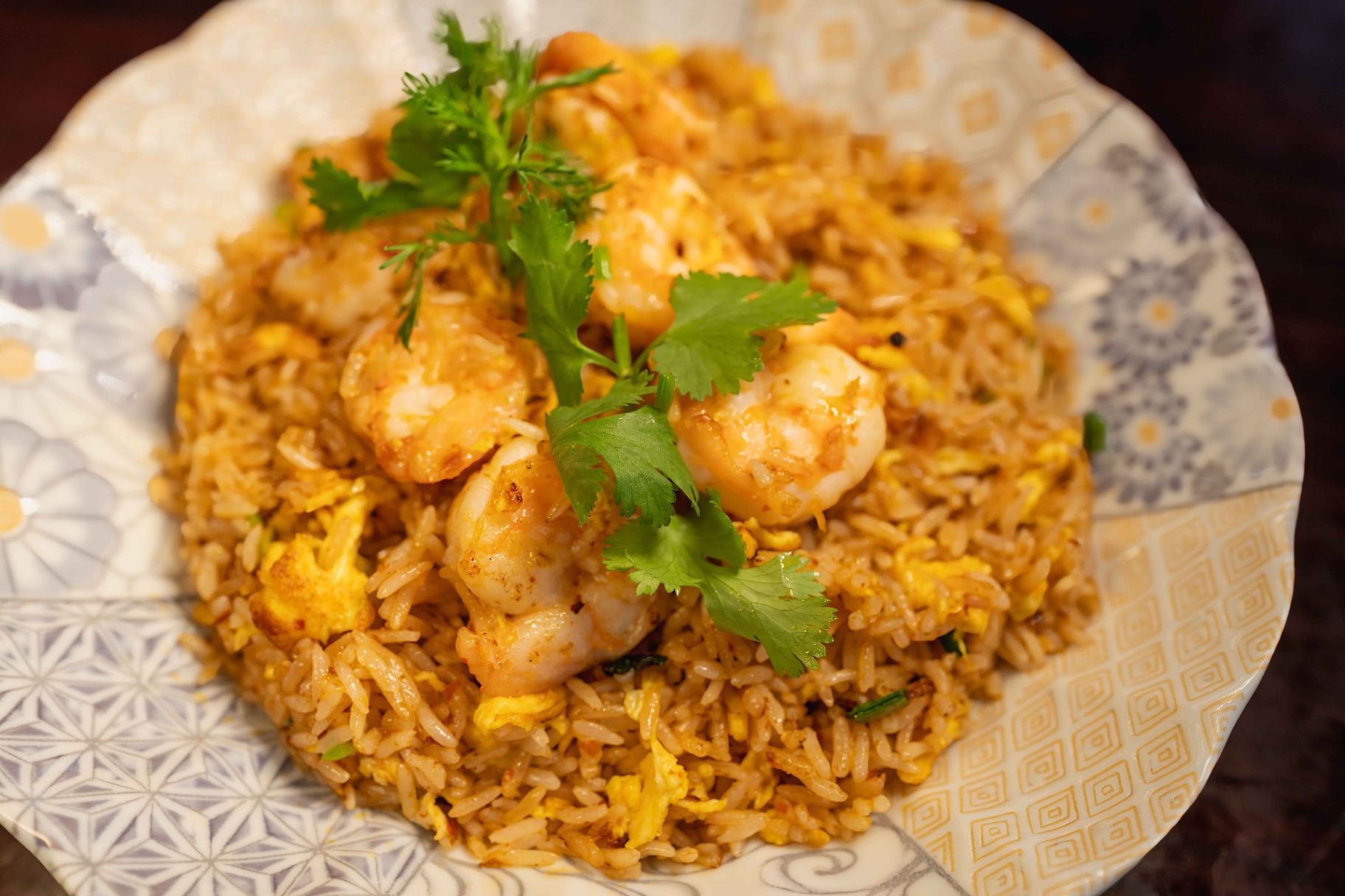 Plate of biryani rice topped with grilled shrimp and fresh cilantro