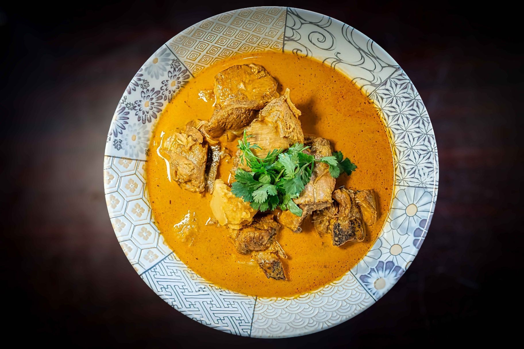 Creamy orange curry in a patterned bowl, garnished with cilantro, on a dark background