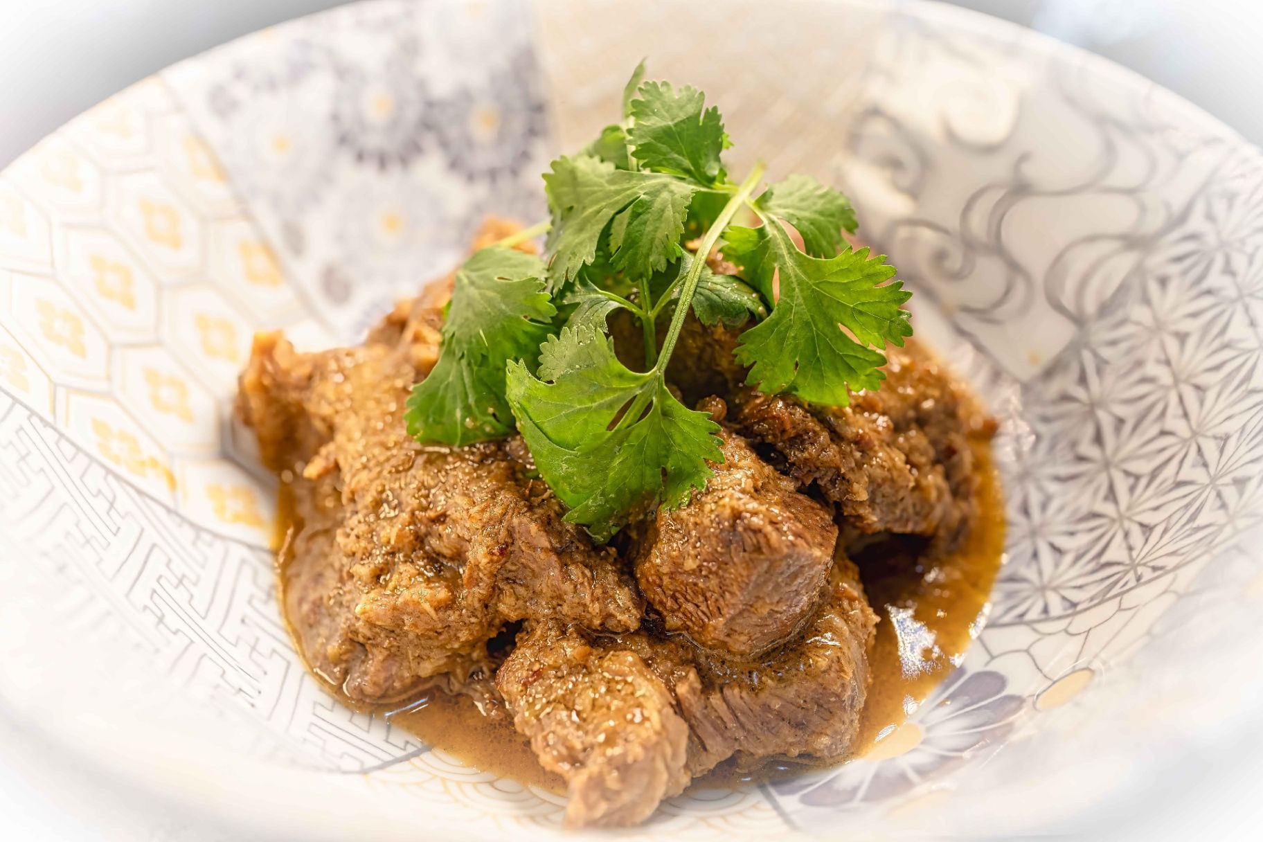 Braised meat chunks garnished with fresh cilantro in a patterned white bowl