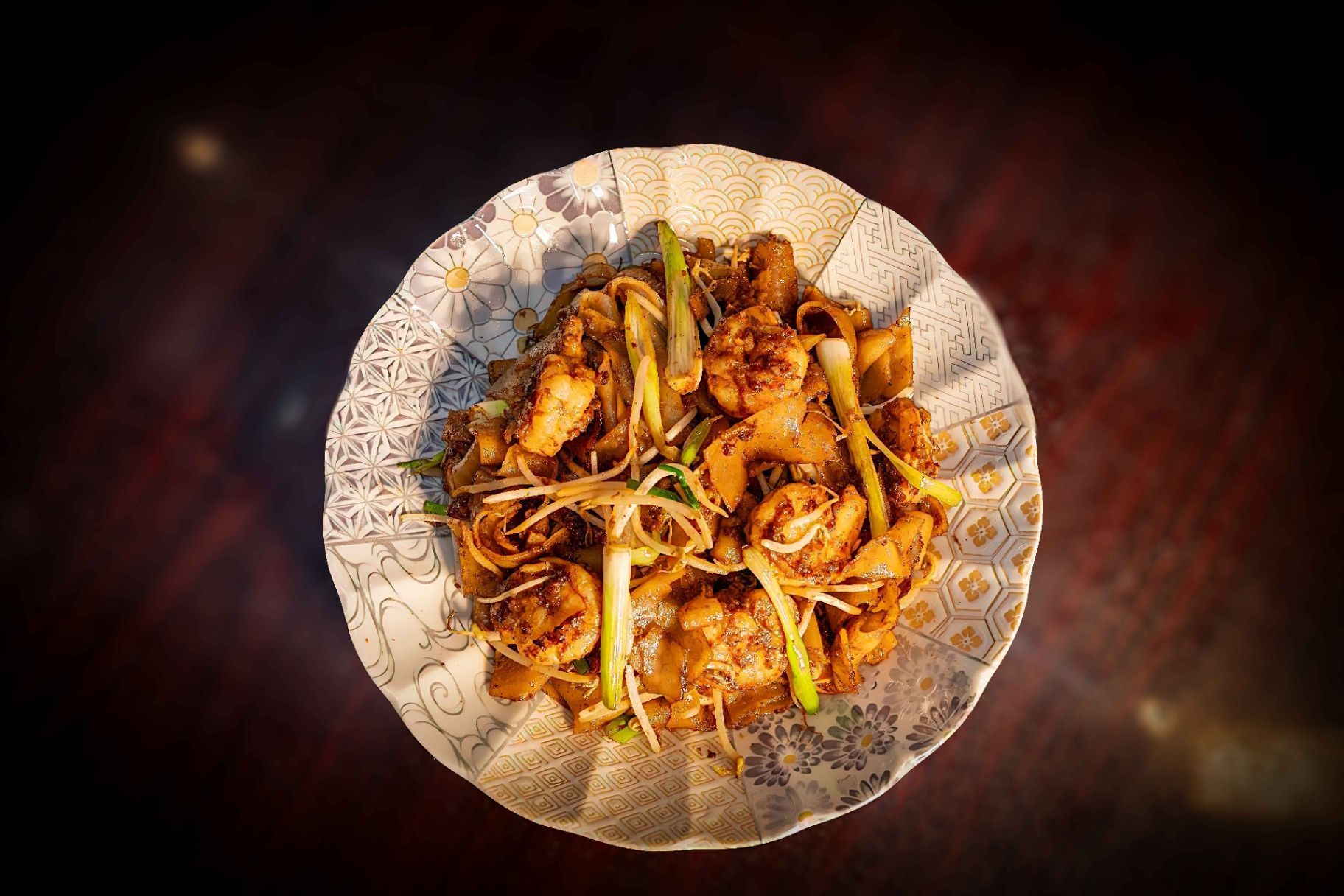 Plate of cooked noodles with vegetables and spices on a patterned dish