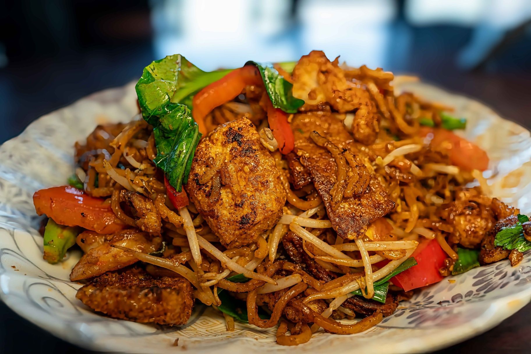 Plate of stir-fried noodles with chicken, bean sprouts, and vegetables on a floral dish