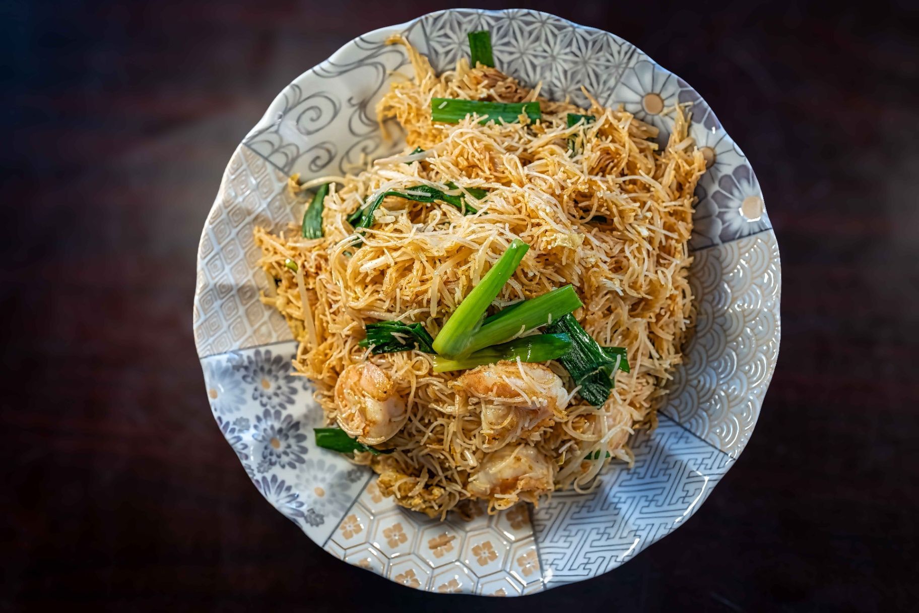 Plate of golden shredded noodles topped with green chilies and herbs on a patterned dish