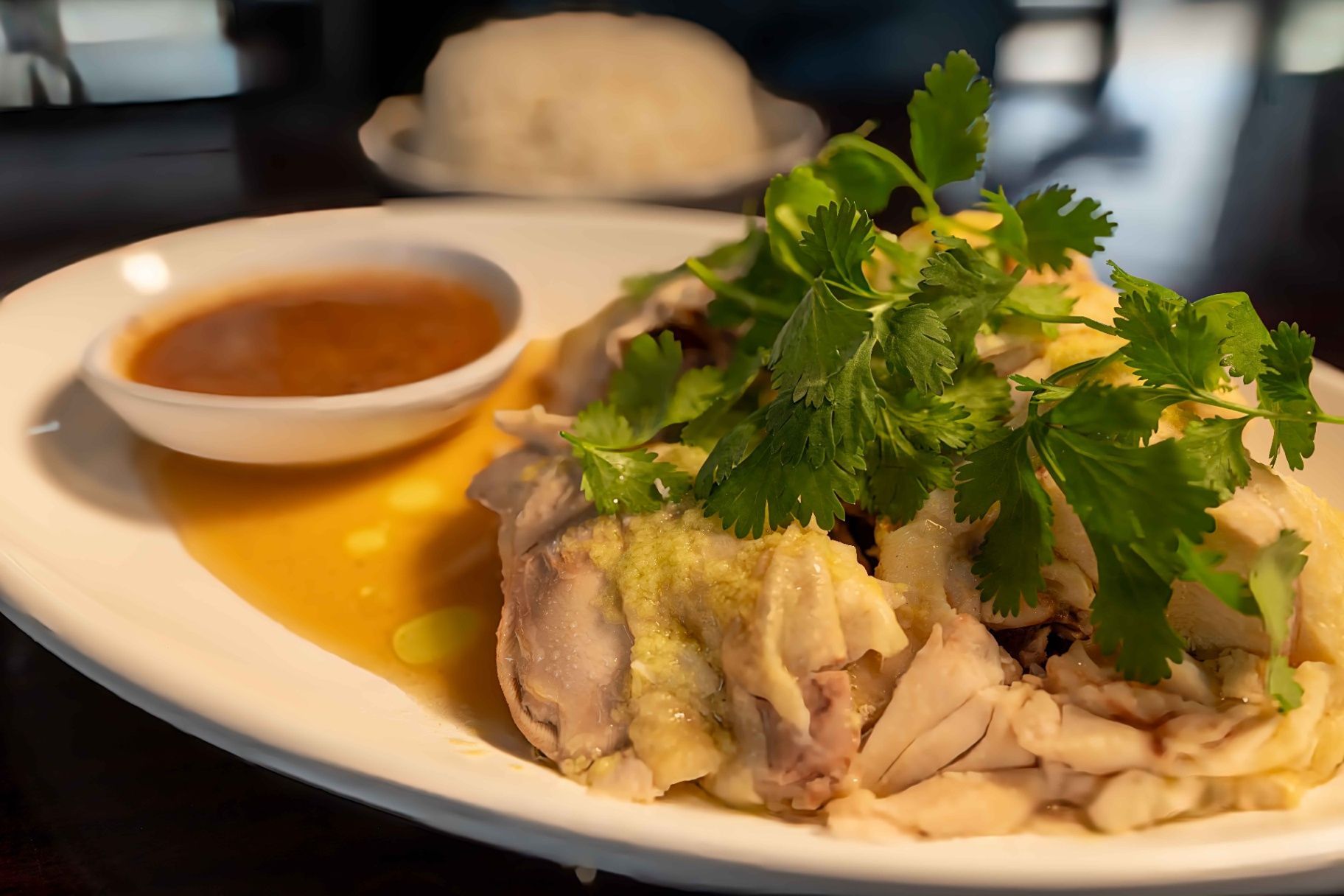 Plate of sliced chicken garnished with cilantro, served with rice and dipping sauce on a table