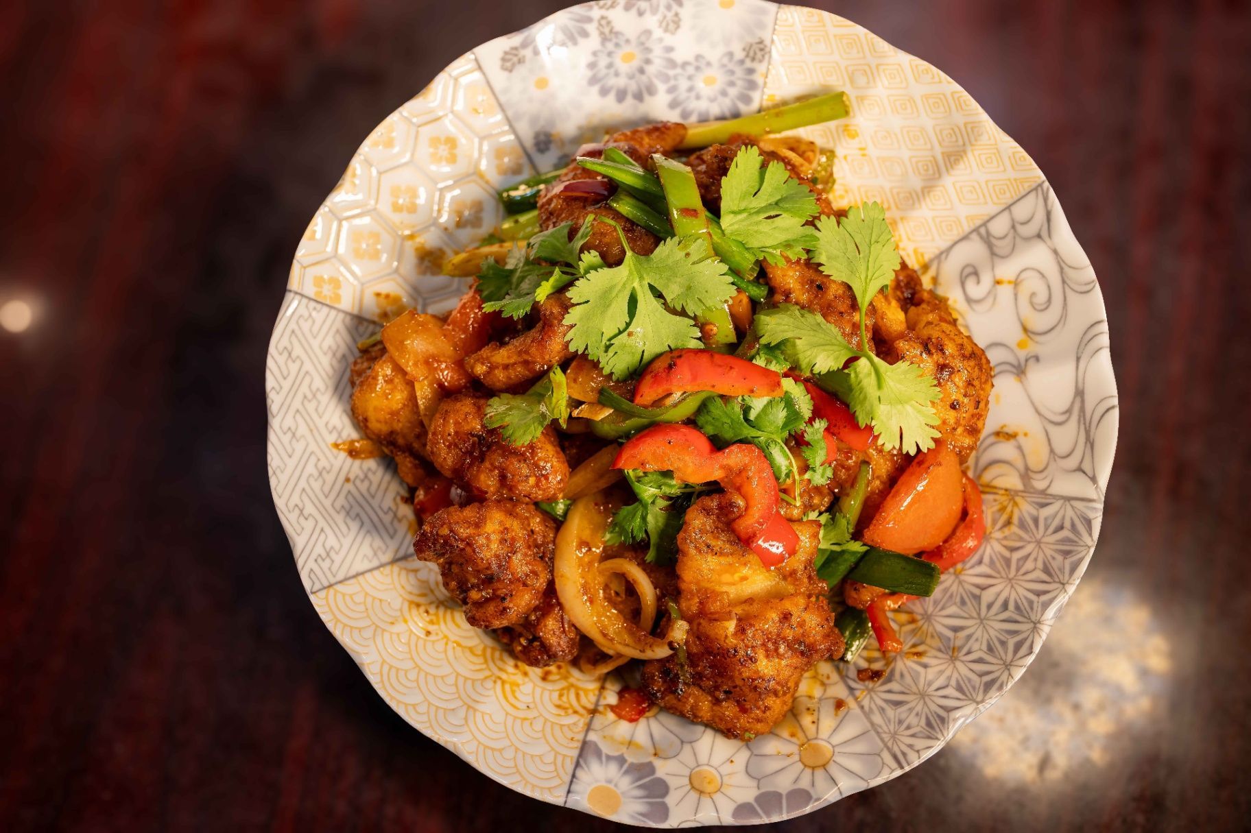 Plate of spicy stir-fried chicken garnished with cilantro and red peppers on a patterned dish