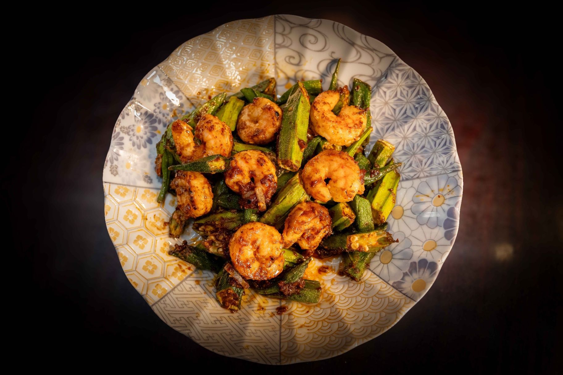 Plate of golden fried bites and green peppers on a patterned dish against a dark background