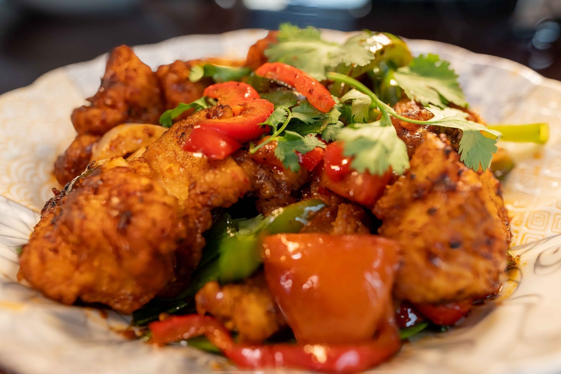 Plated fried chicken pieces with red peppers, cilantro, and vegetables in a saucy dish