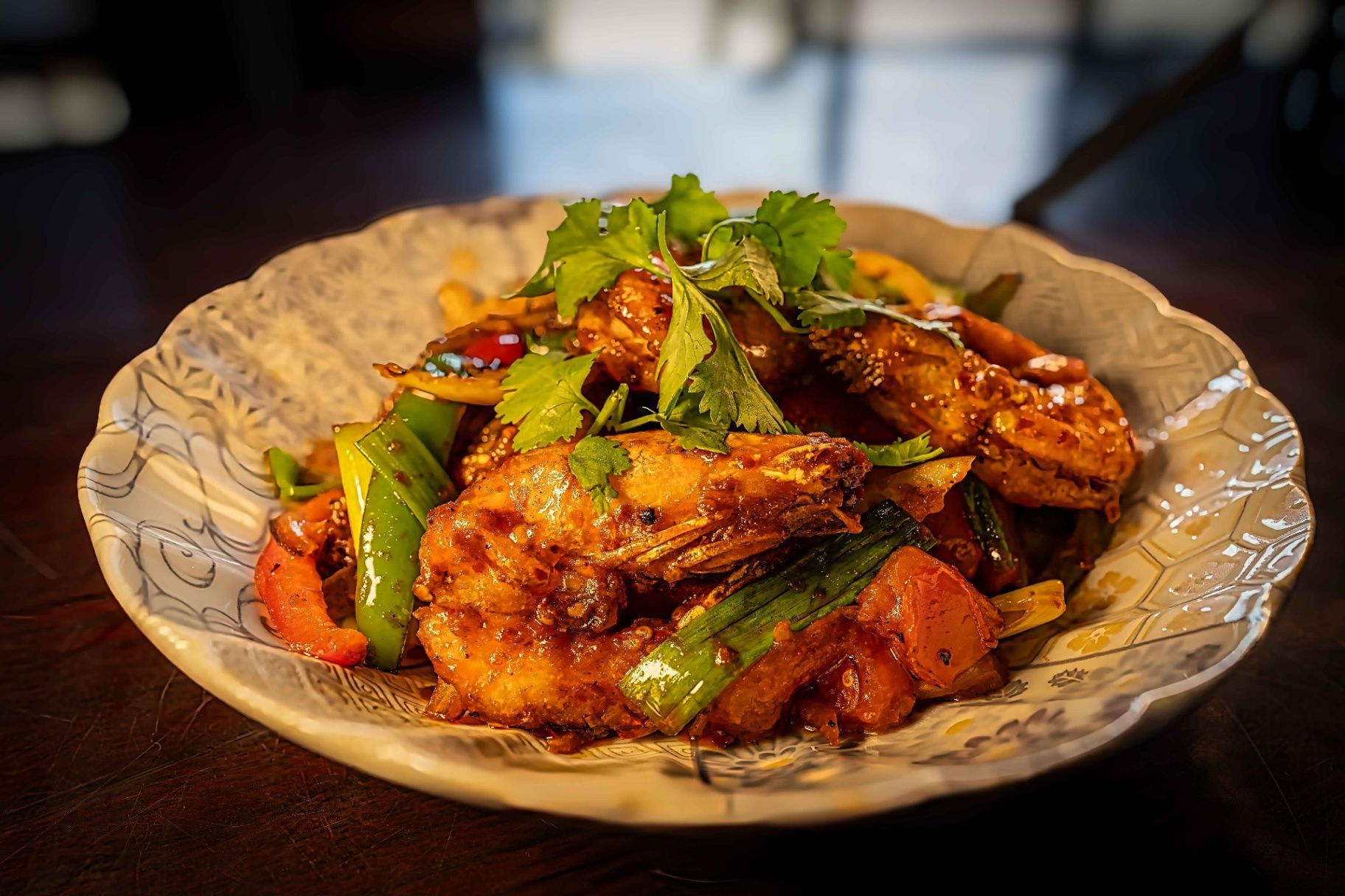 Glazed chicken wings topped with chopped green onions on a patterned plate
