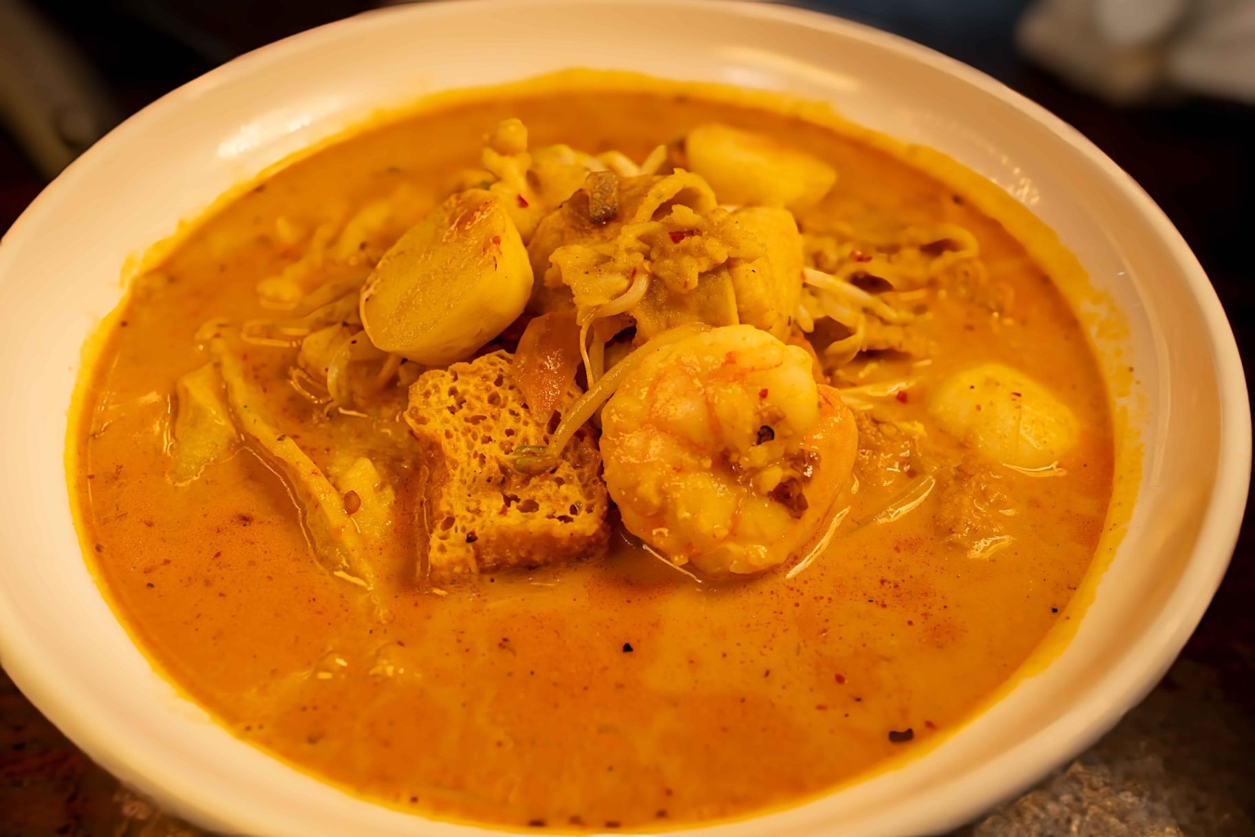 Bowl of creamy orange soup with shrimp and dumplings, served on a table