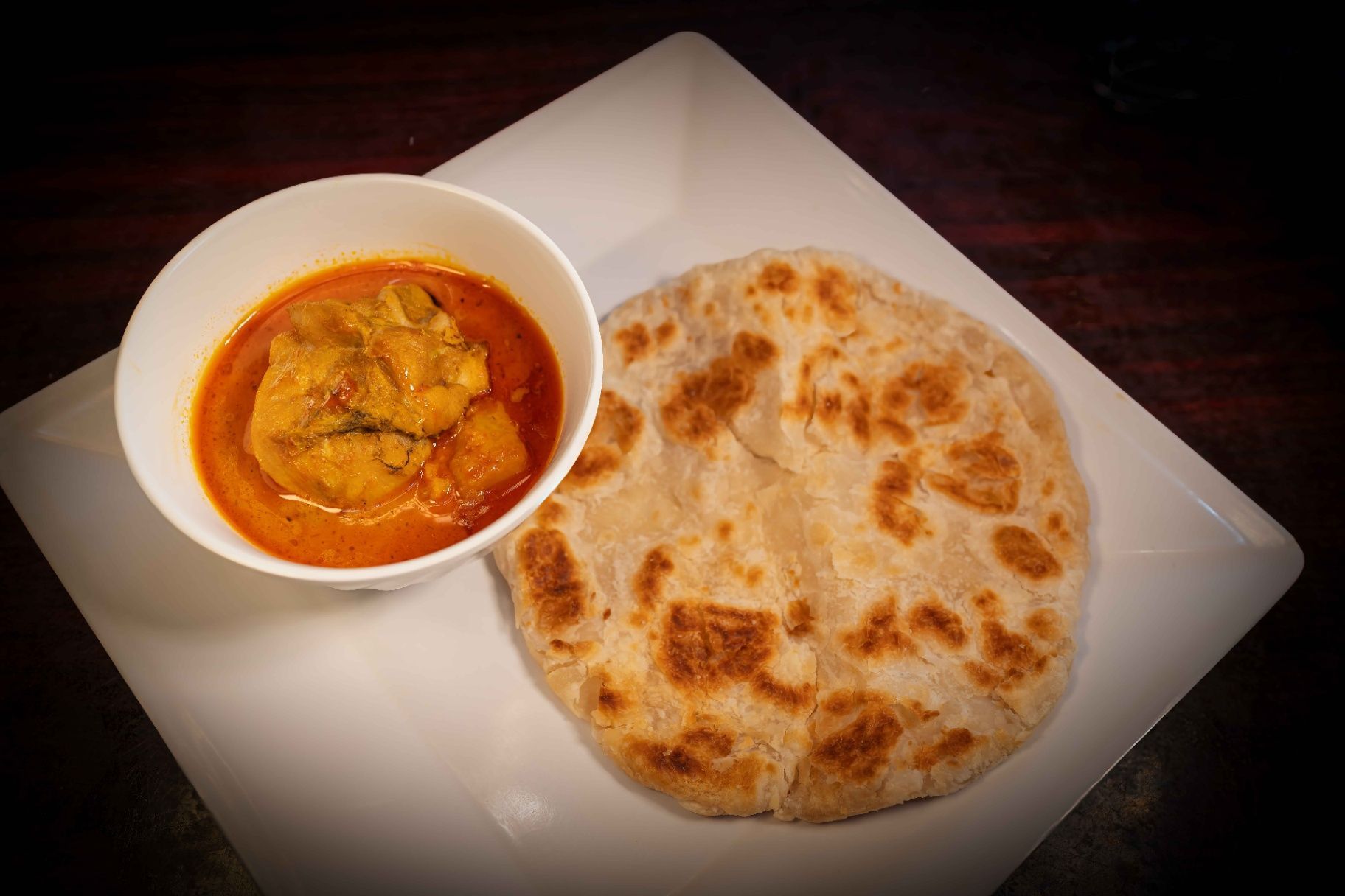 Plate of naan with curry in a white bowl on a square plate