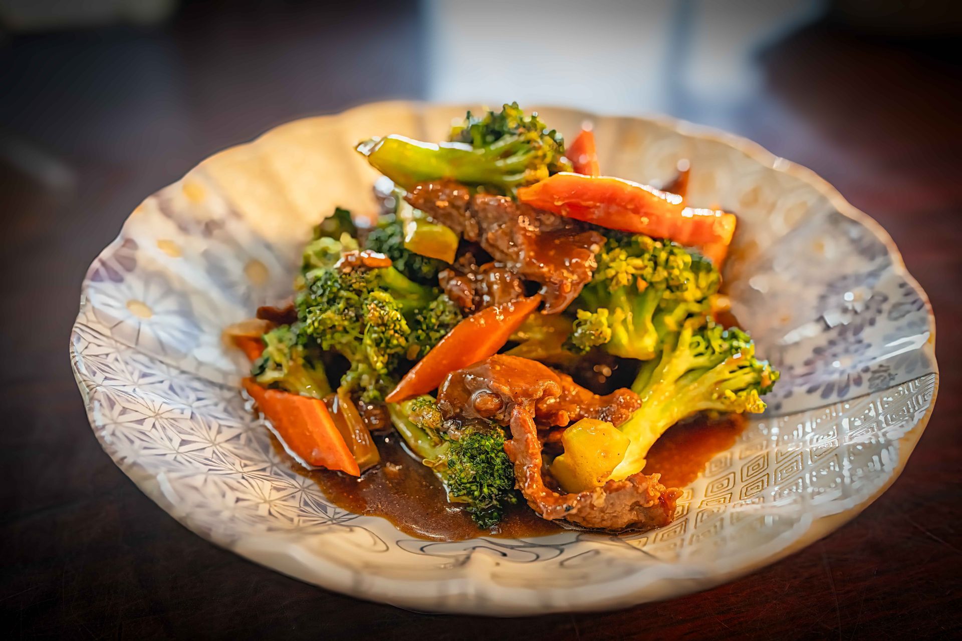 Broccoli and carrot stir-fry in sauce on a patterned white plate