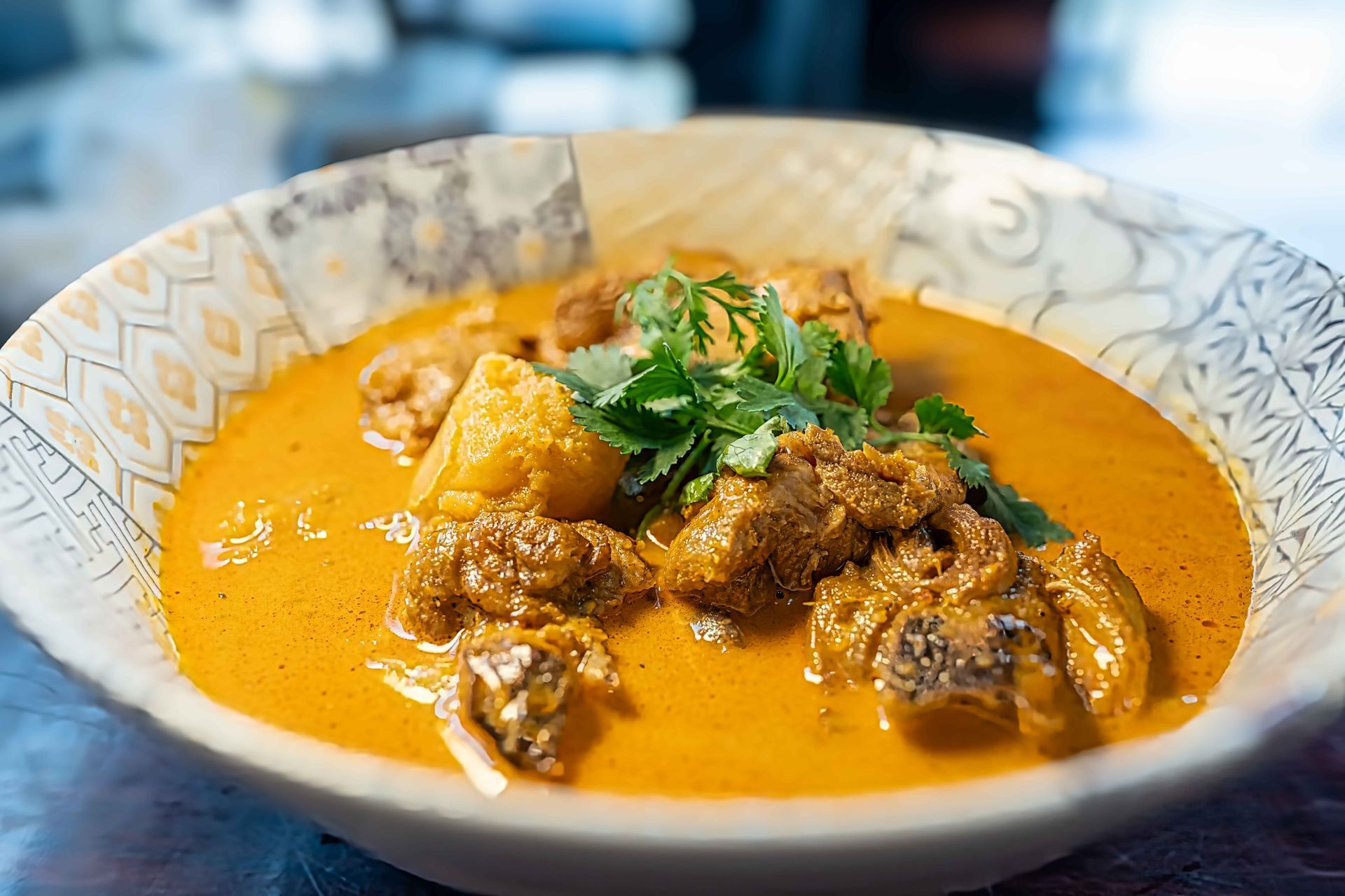 Bowl of creamy orange curry with meat, garnished with cilantro