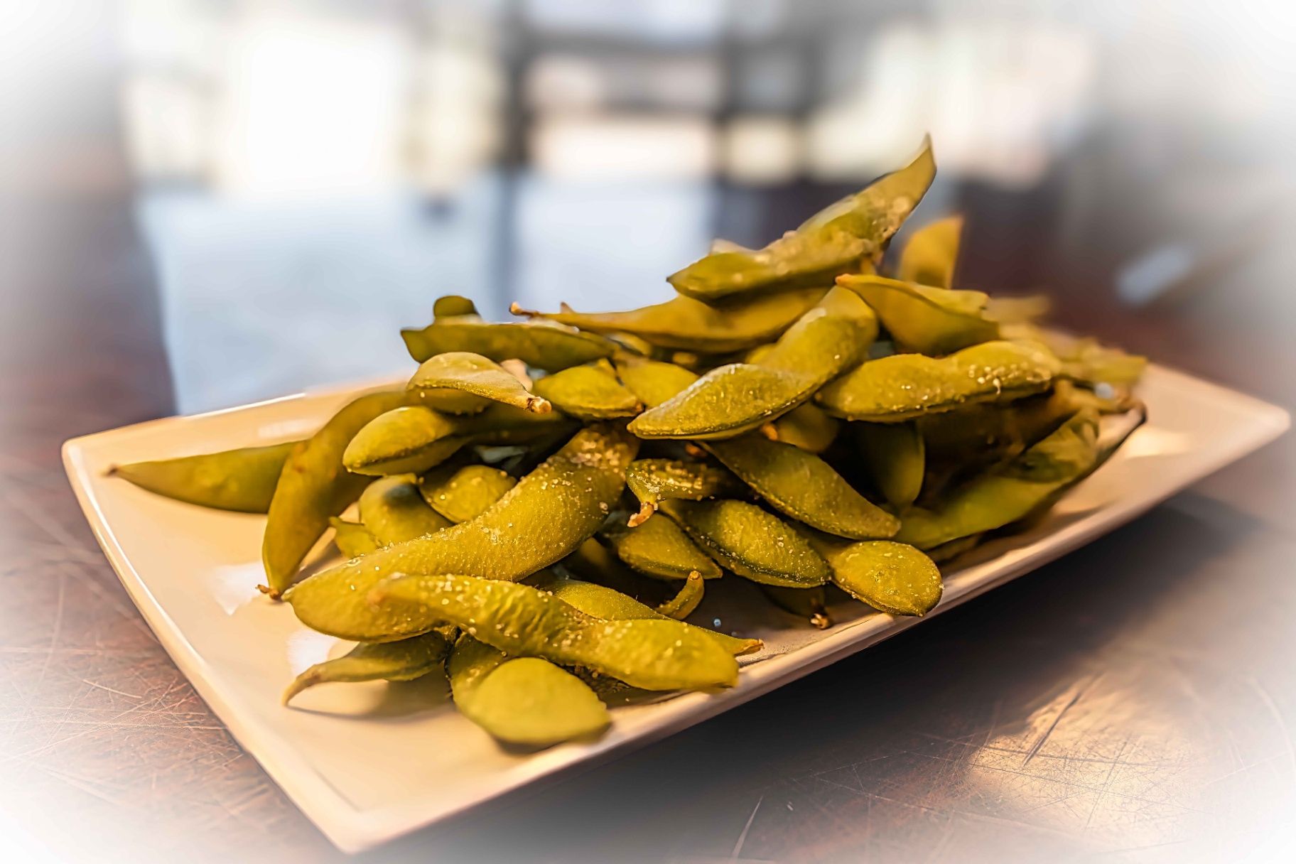 Plate of salted edamame pods on a table in a blurred restaurant setting