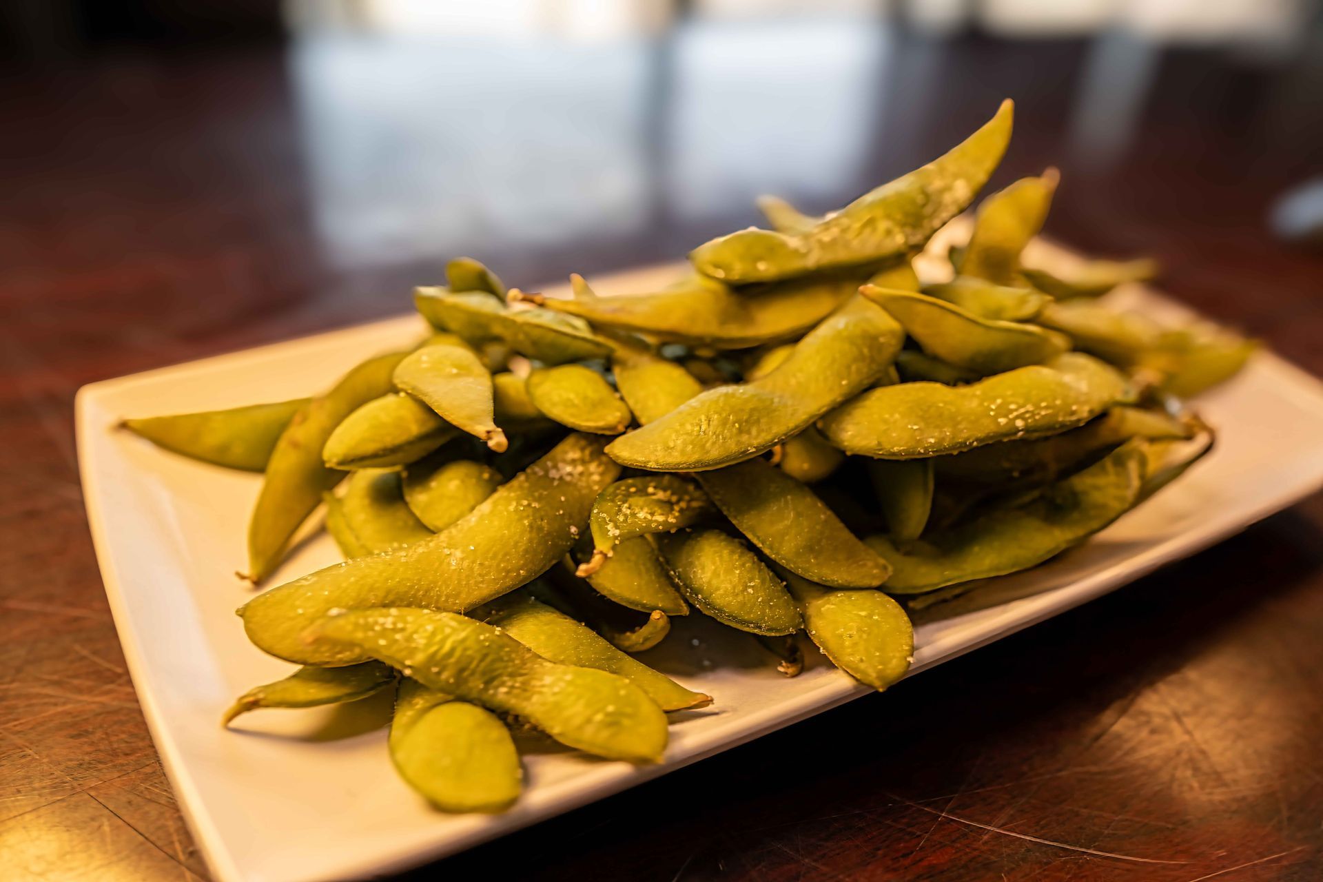 Plate of salted edamame pods on a wooden table