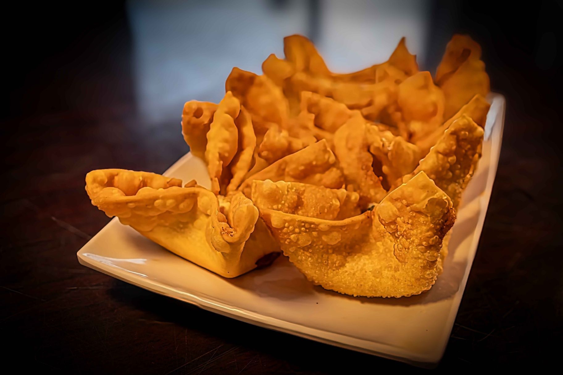 Golden fried wontons on a white plate against a dark background