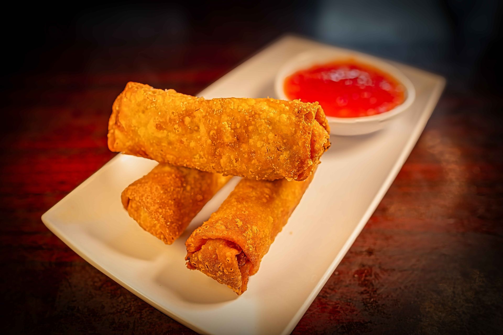 Three golden fried spring rolls on a plate with red dipping sauce
