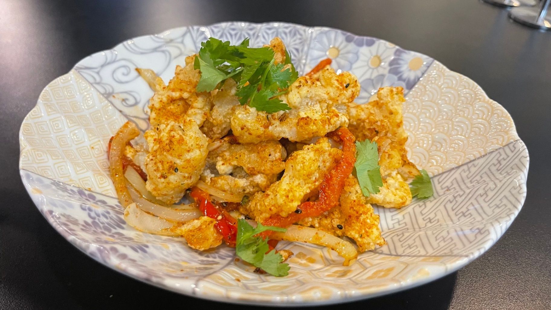 Plate of crispy fried food garnished with cilantro and red pepper flakes in a patterned bowl