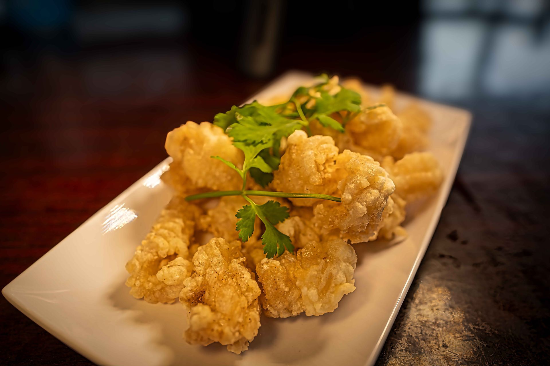 Fried cauliflower florets garnished with parsley on a white rectangular plate
