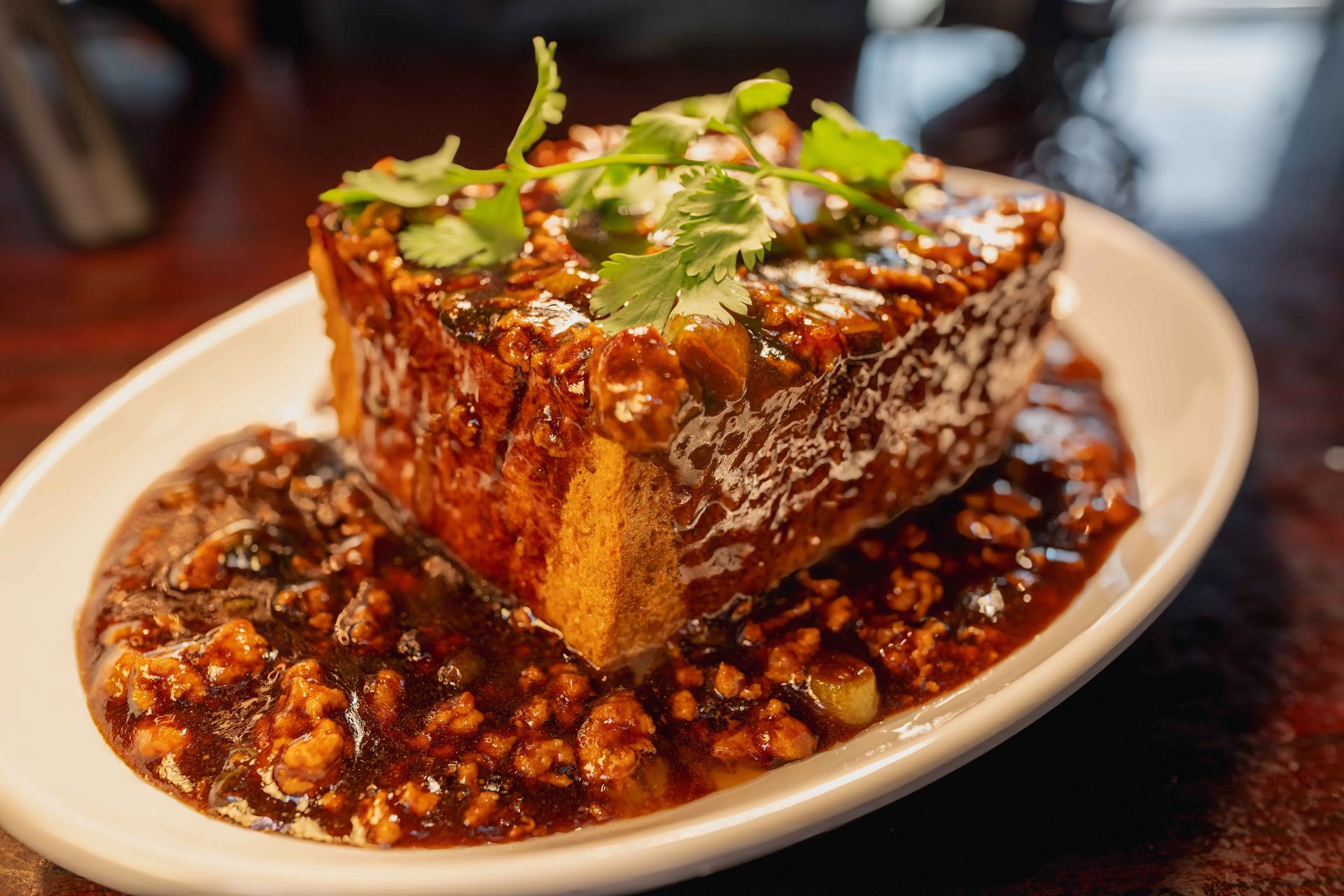 Tofu block with savory sauce and green garnish on a white plate