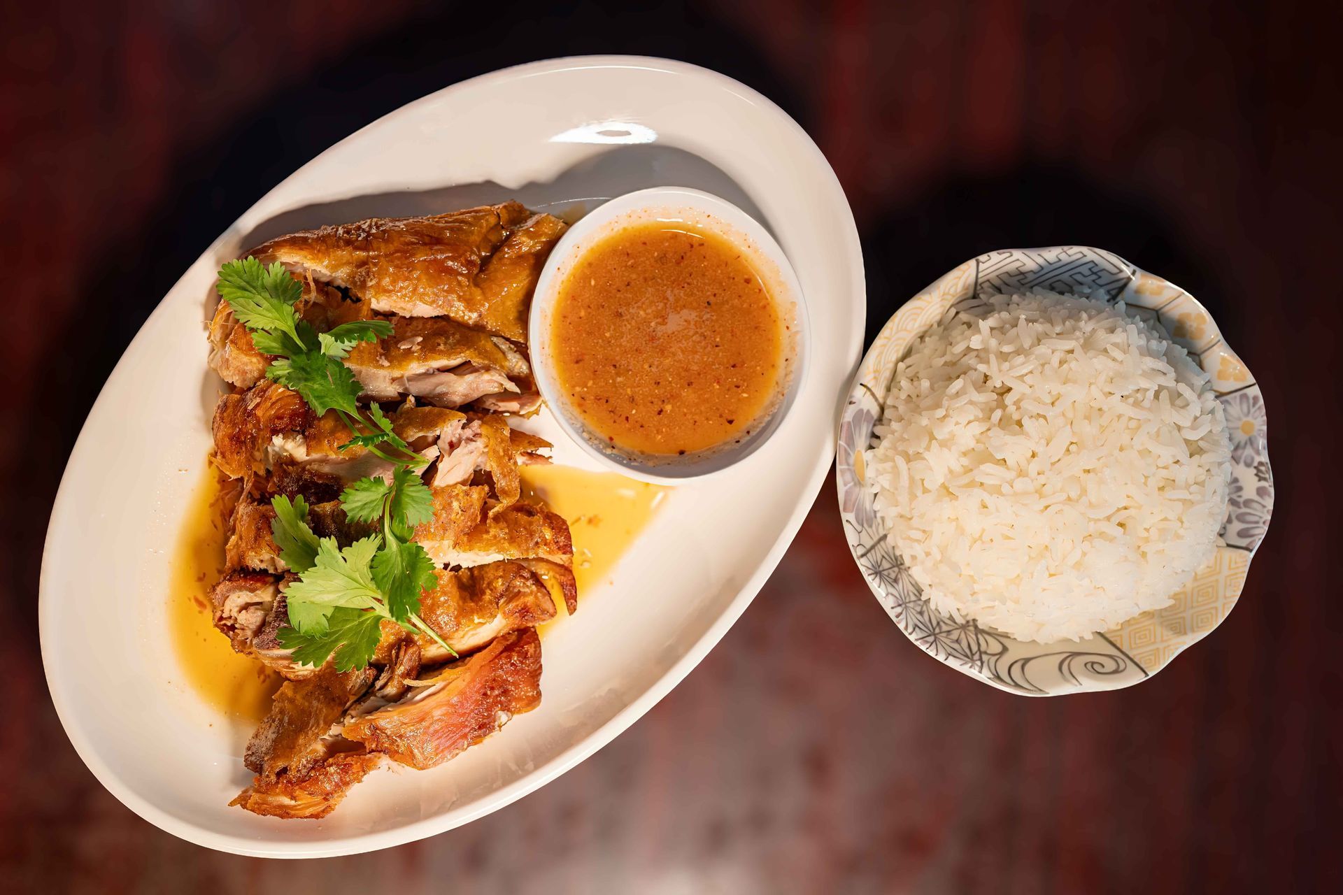 Grilled chicken on a white plate with sauce and rice on a wooden table