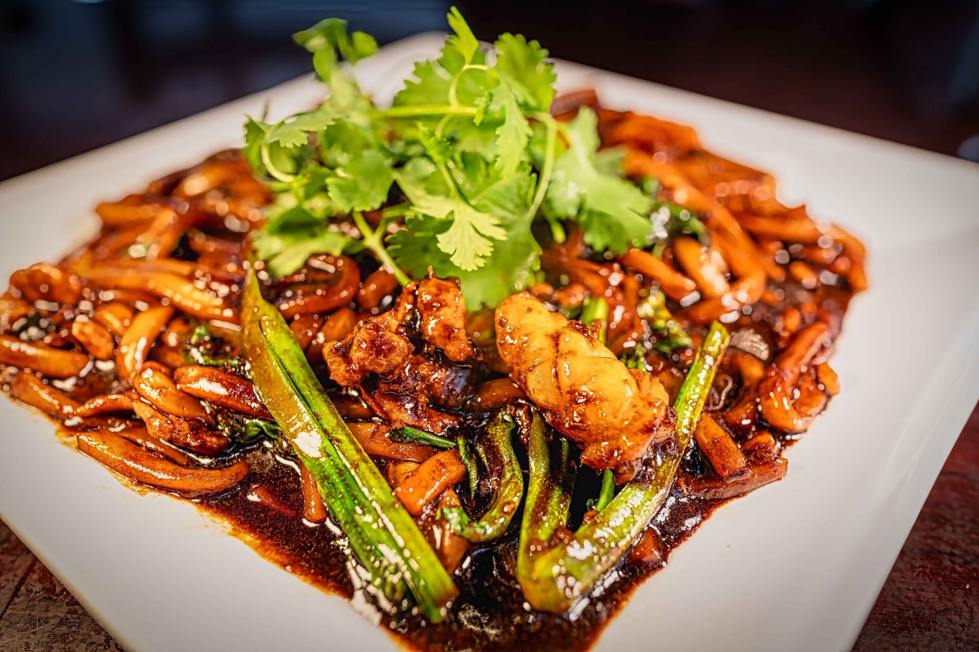 Stir-fried noodles with shrimp and greens on a white plate, garnished with cilantro