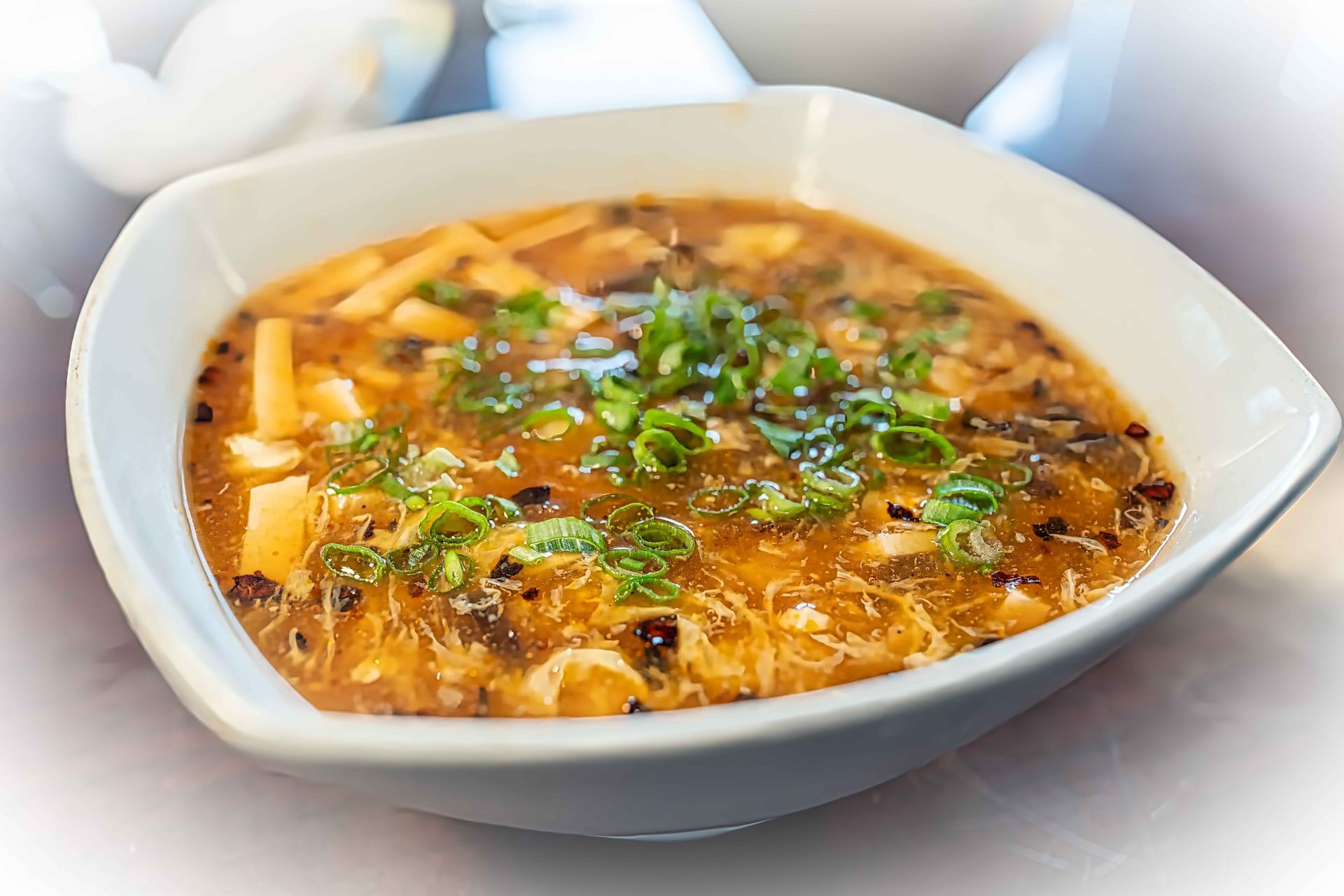 White bowl of hot soup topped with herbs and shredded cheese on a table