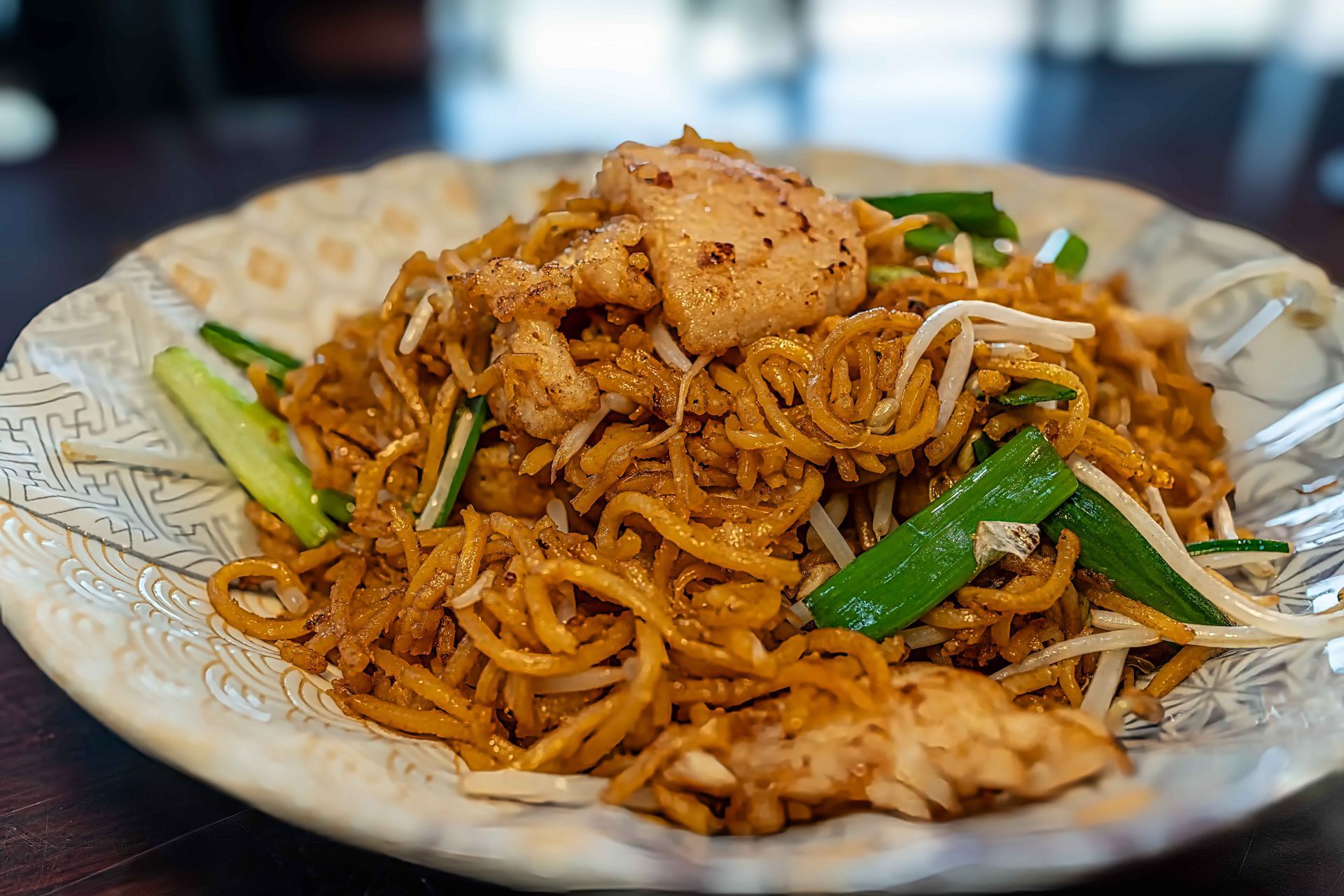 Plate of stir-fried noodles topped with chicken and green vegetables