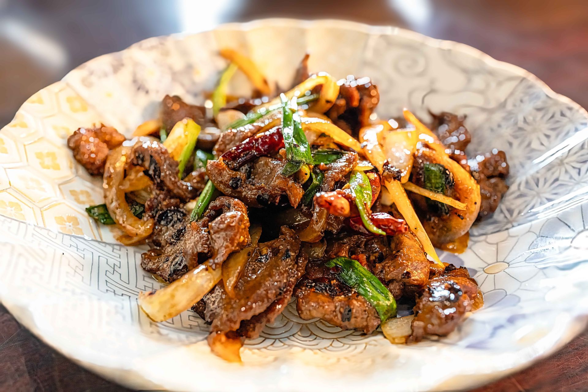 A bowl of stir-fried noodles with vegetables and meat, garnished with herbs and chili peppers.