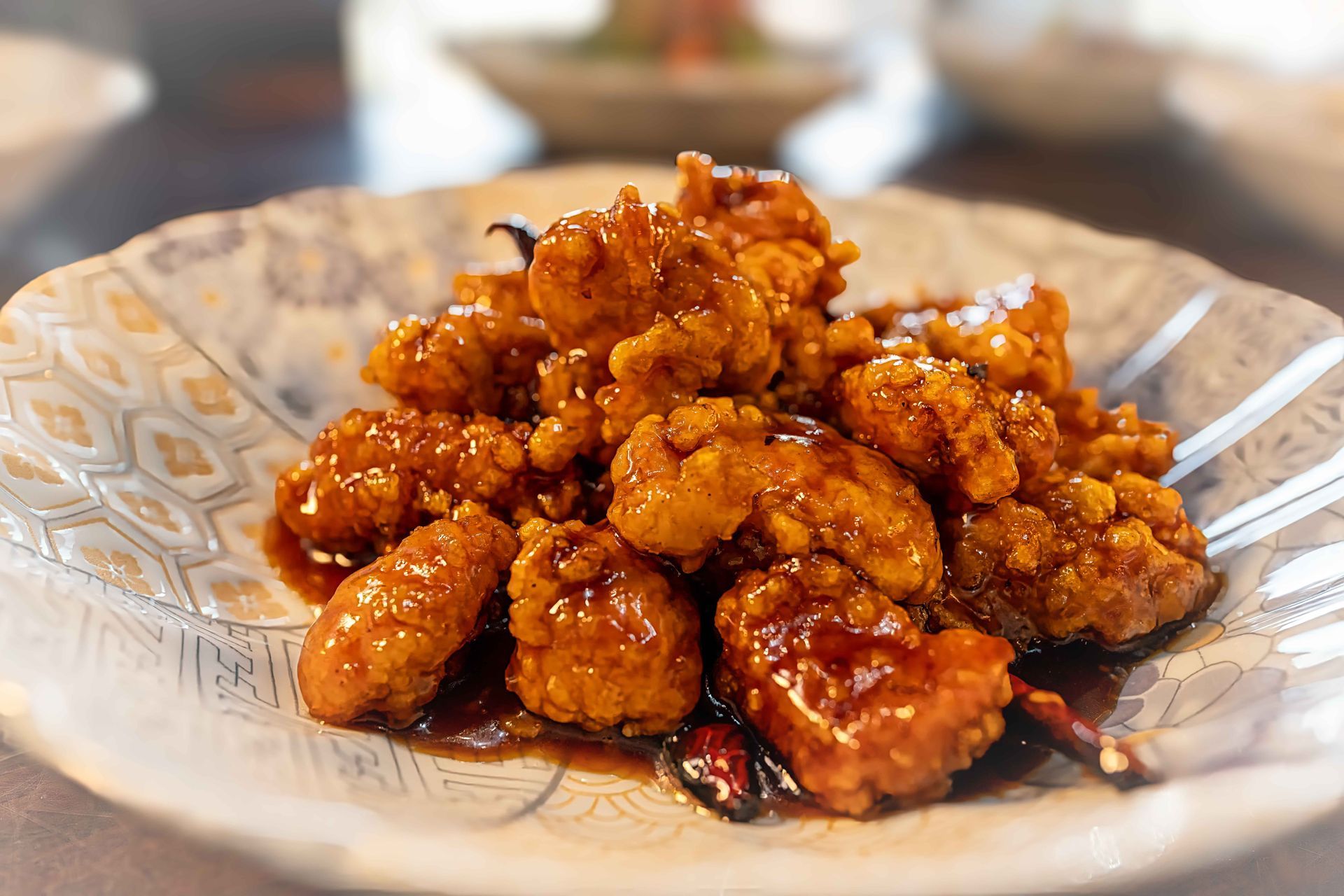 Close-up of glazed fried chicken pieces on a patterned white plate