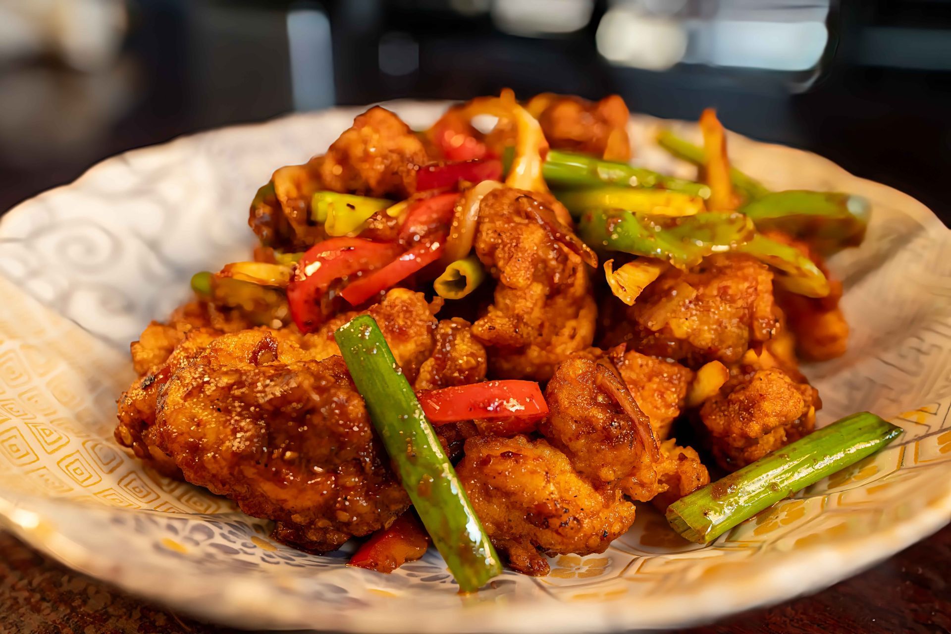 Plate of crispy fried chicken with red and green peppers on a patterned dish