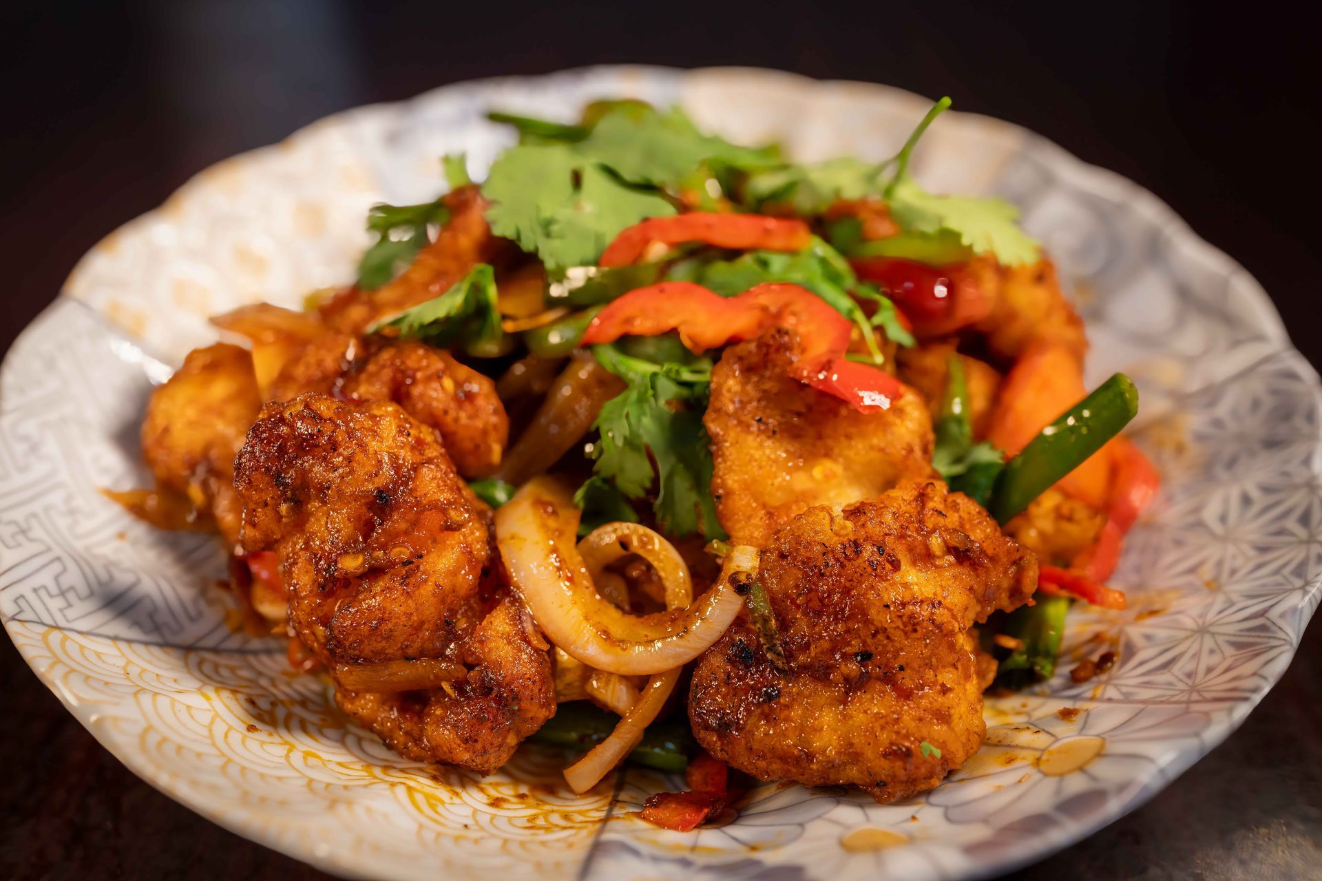 Plated spicy fried chicken with onions and red peppers on a patterned dish