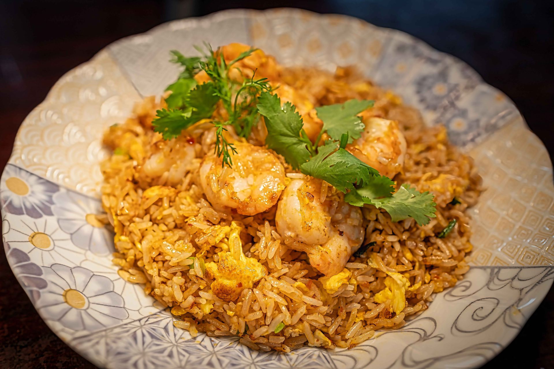 A plate of spiced rice topped with shrimp, garnished with cilantro.