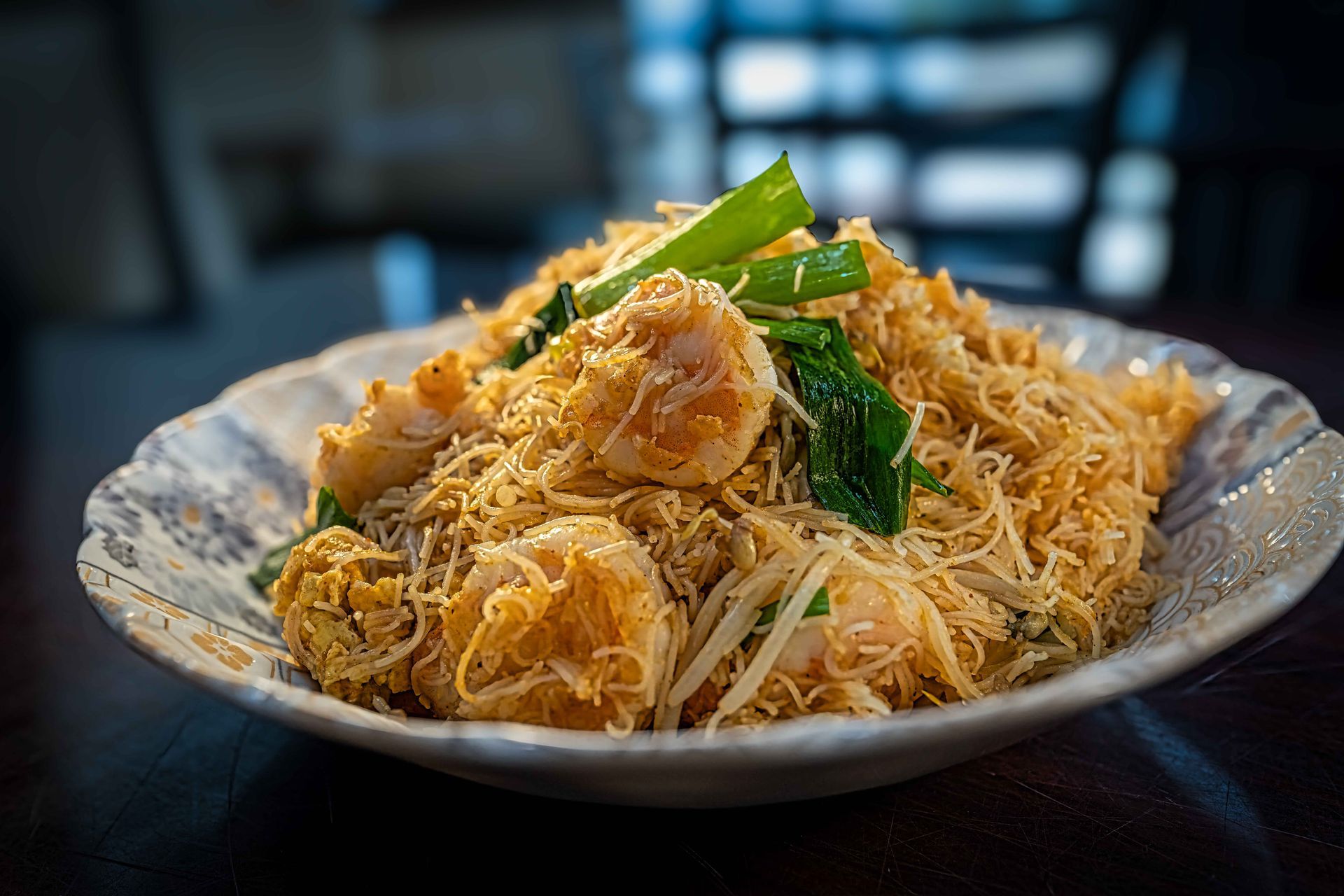 Plate of fried noodles with chicken and green onions on a patterned dish