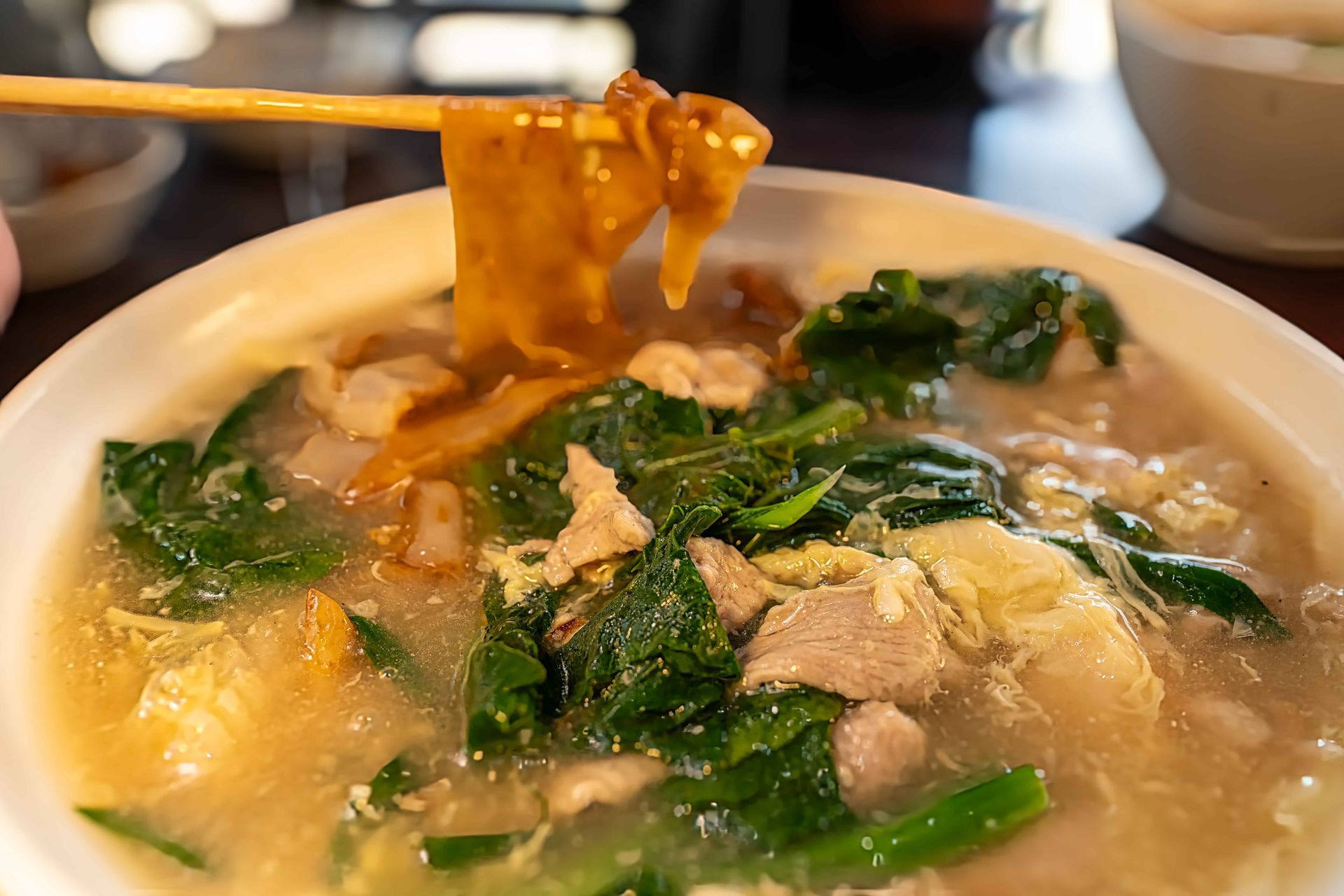 Close-up of a steaming bowl of noodle soup with greens, meat, and tofu