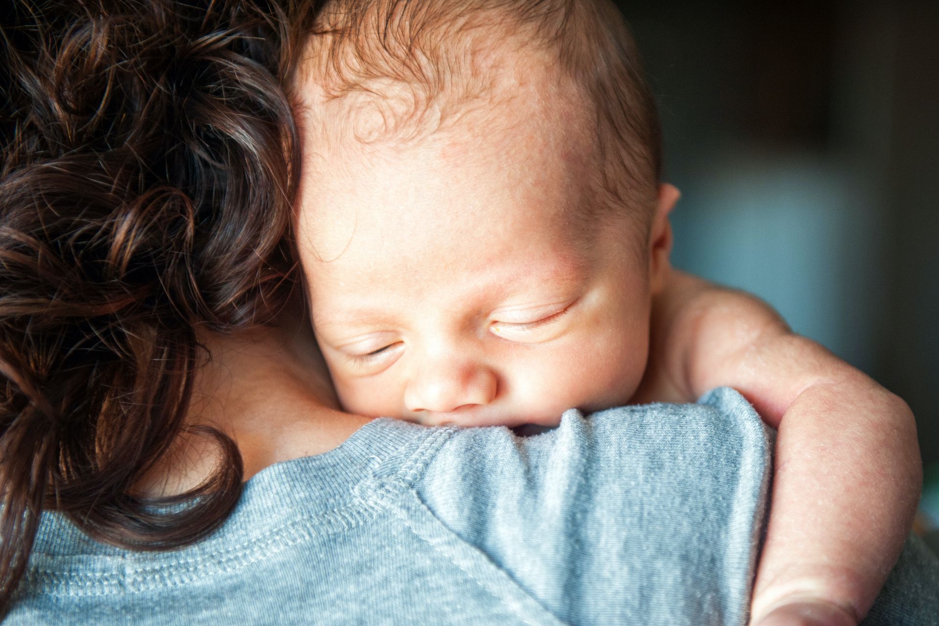 Newborn baby sleeping peacefully on a person's shoulder, close up, indoor setting.