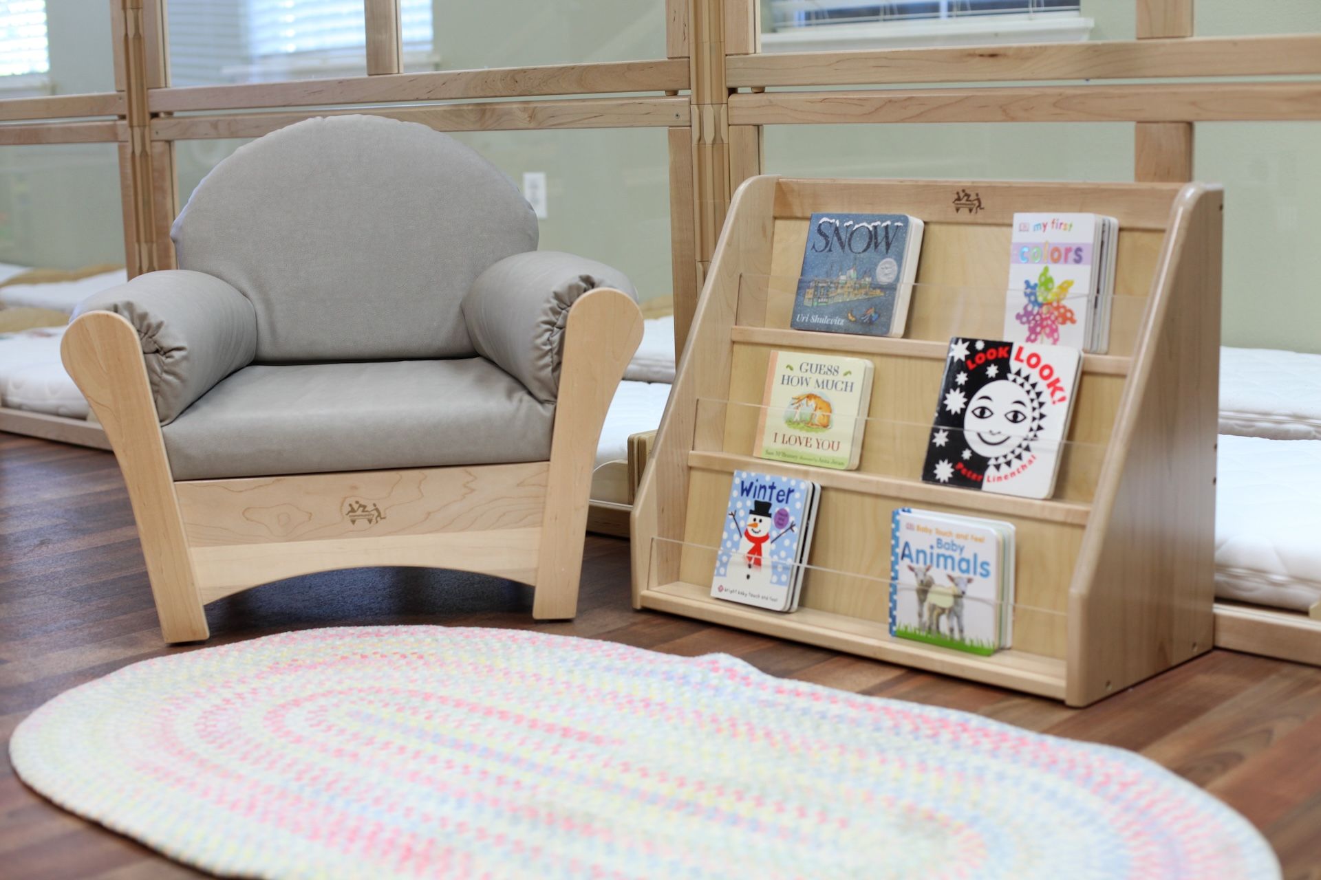 Reading nook with a gray armchair, bookshelf with books, and oval rug.