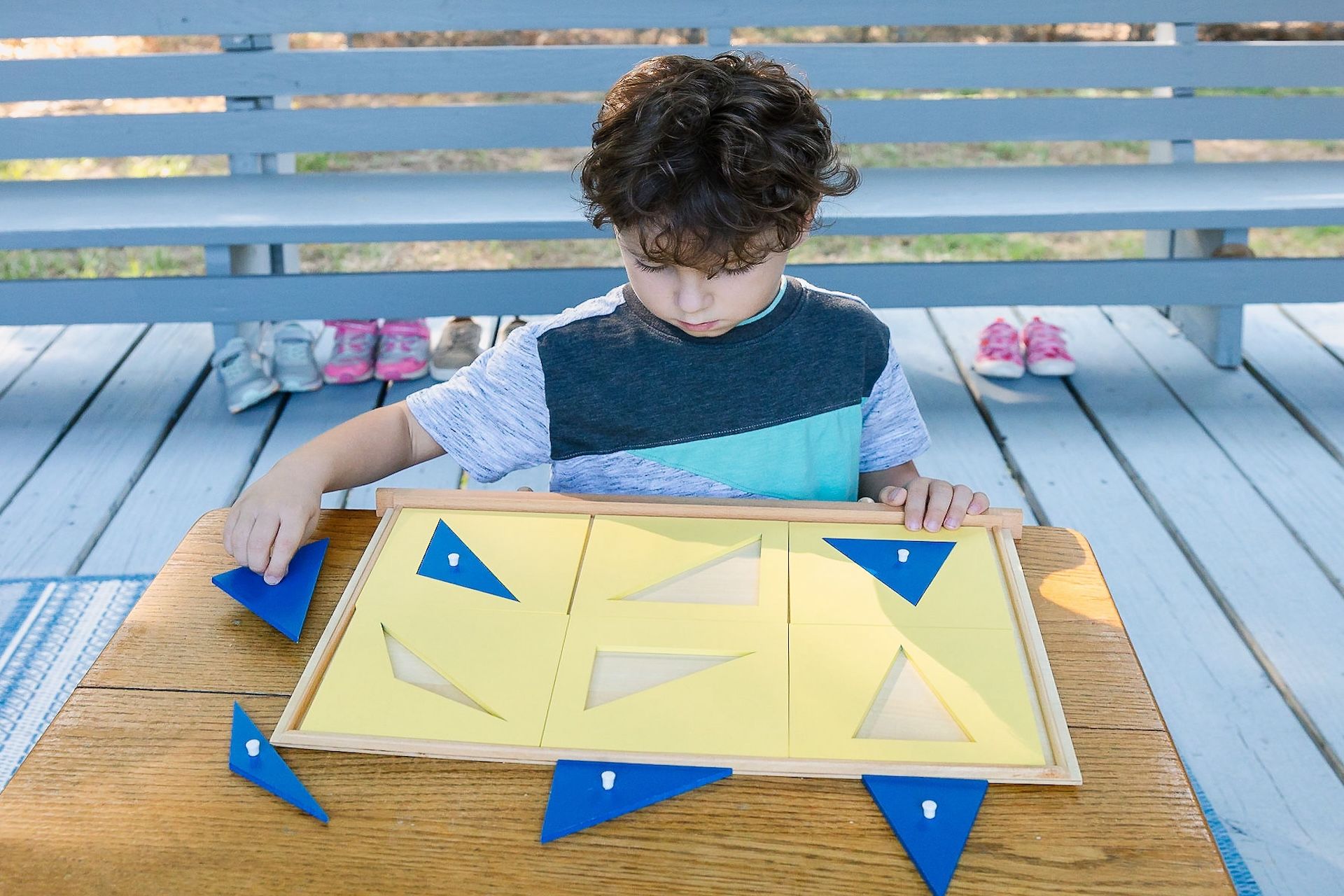 Boy playing with wooden puzzle containing blue triangles.