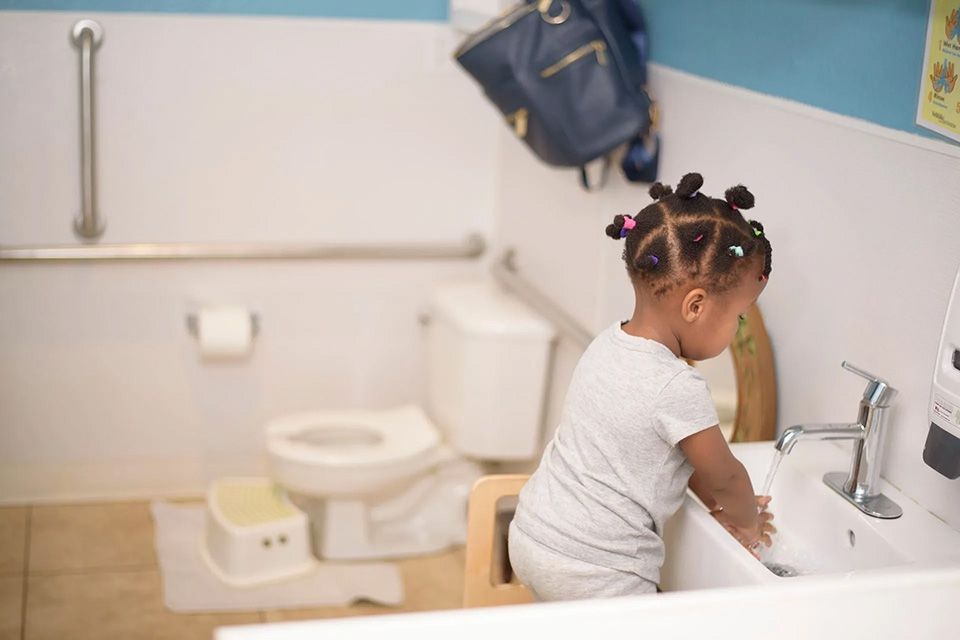 Child washing hands in a bathroom with a child-sized toilet and step stool.