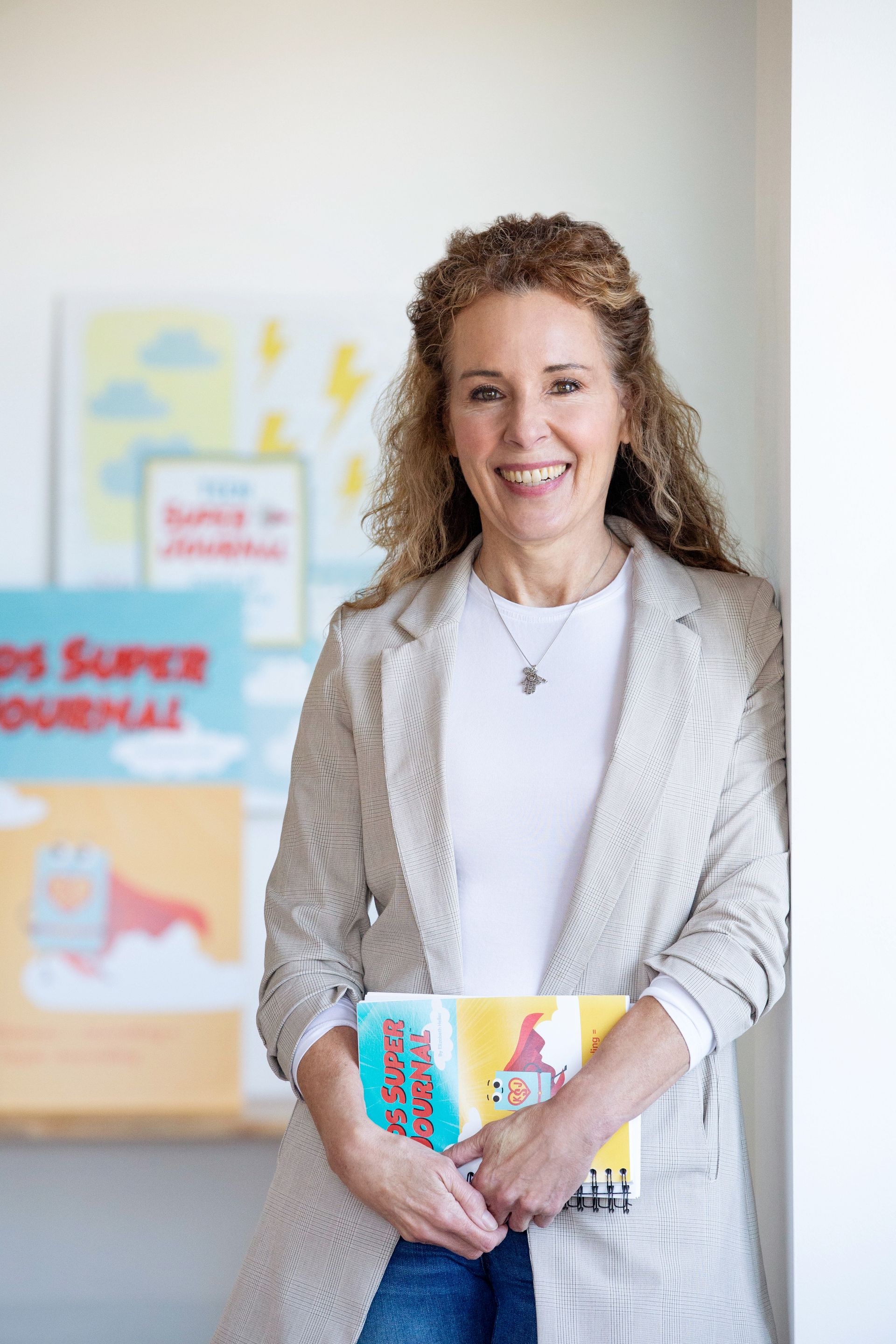 Woman with curly hair smiles, holding books in front of a colorful book display.