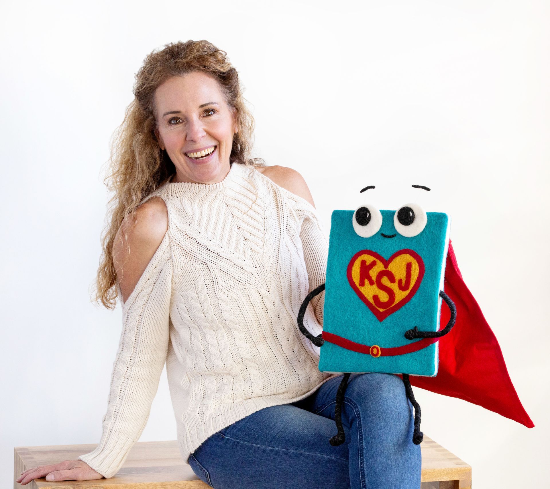 Woman with curly hair and cold shoulder sweater smiles with a book character wearing a cape.